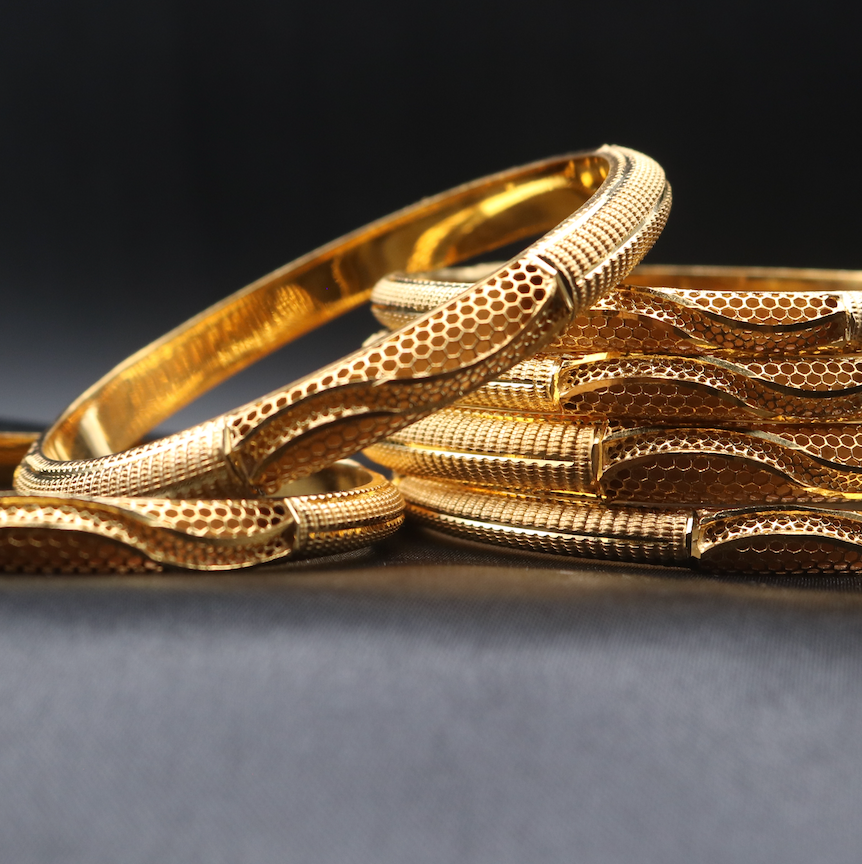 another view of A set of 22k gold-plated bangles with a textured surface, displayed against a dark background.