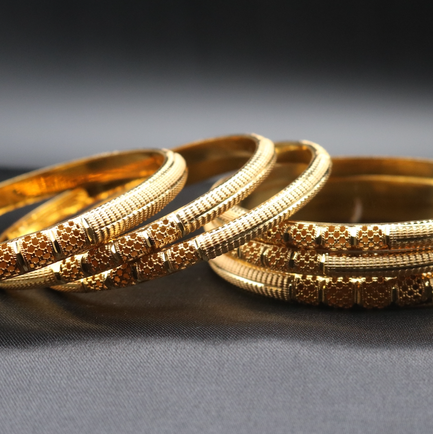 A set of 22k gold-plated bangles with a textured surface, laying flat displayed against a dark background.