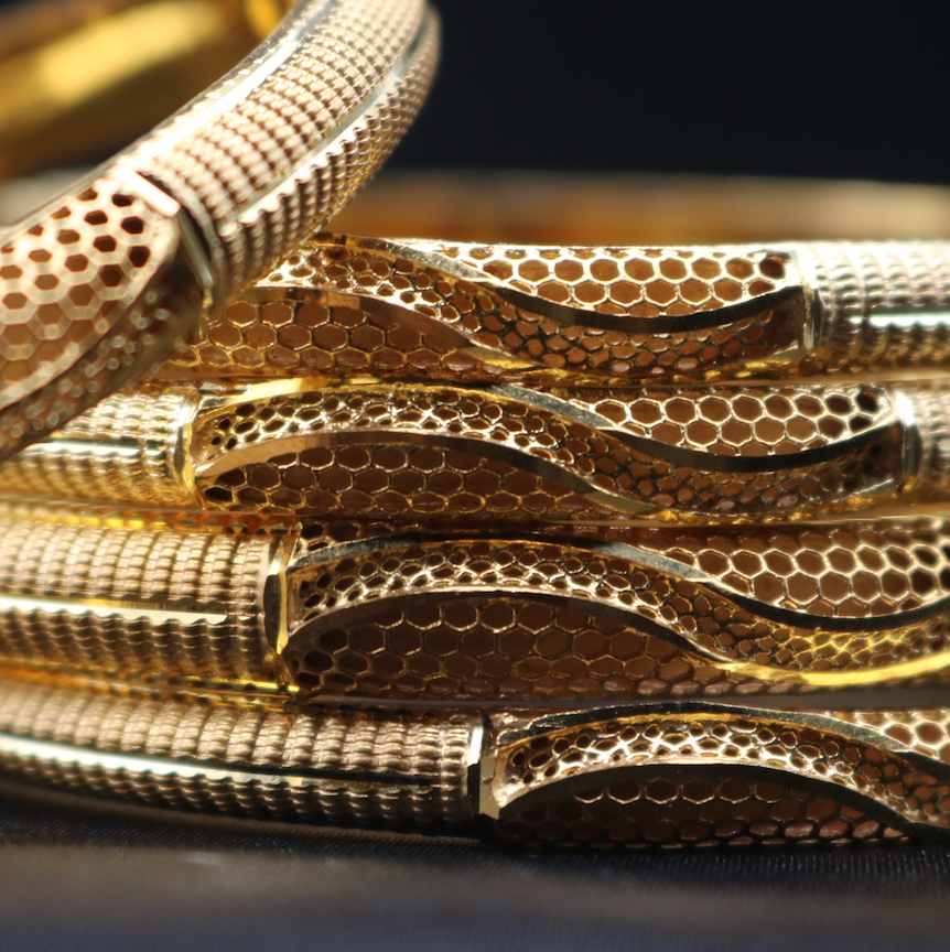 A closer view of a set of 22k gold-plated bangles with a textured surface, displayed against a dark background.