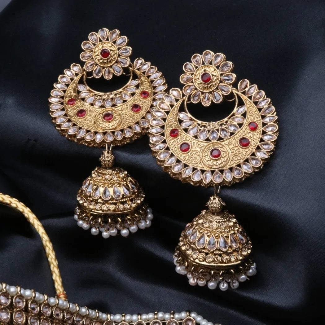 Ornate gold-plated jhumka earrings with red and clear gemstones on a dark background