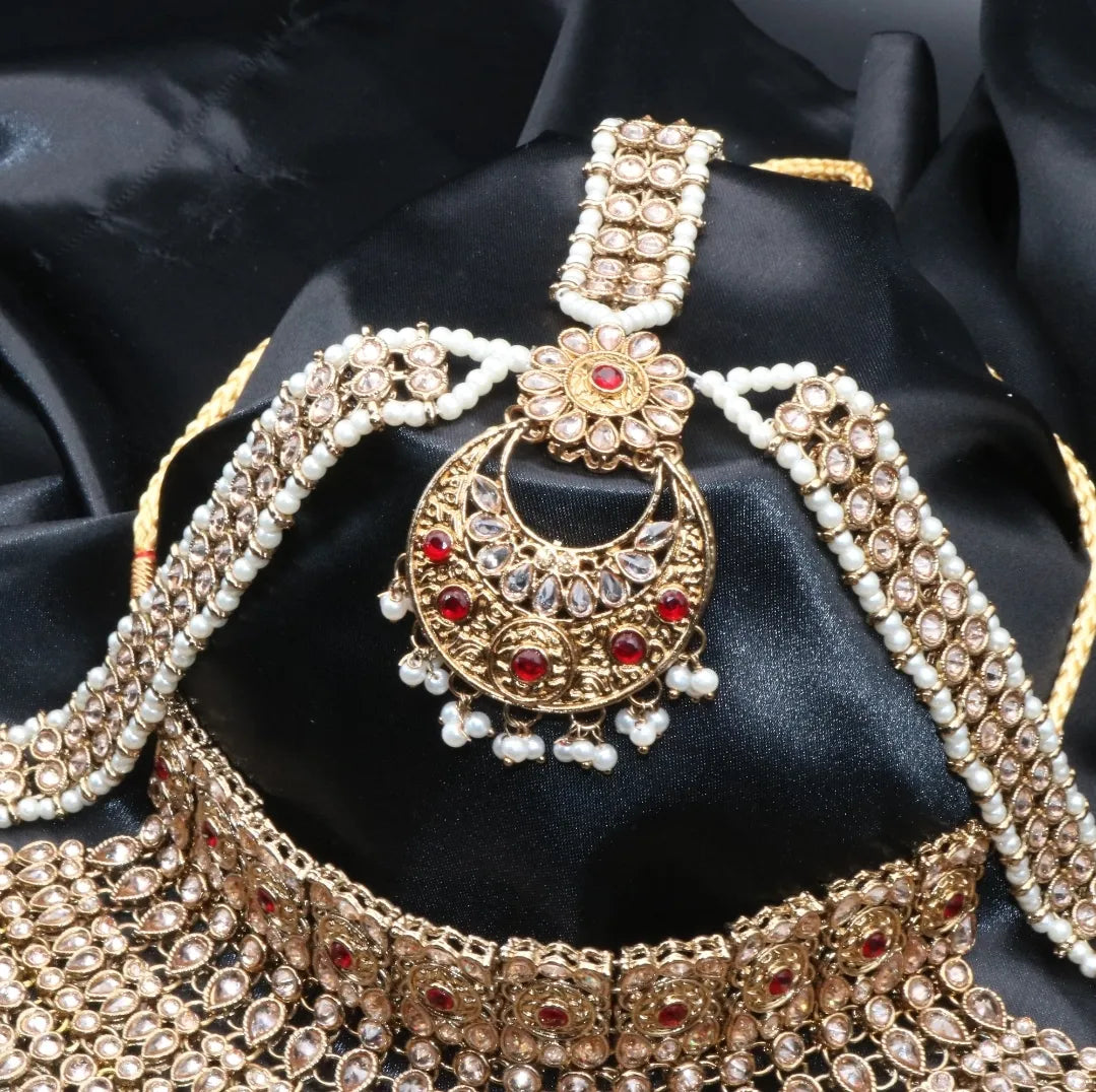 Ornate gold-plated matha patti and red gemstone necklace on black fabric