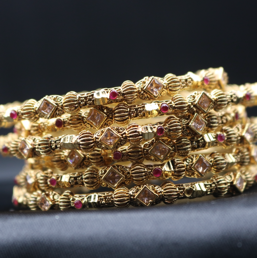 A set of gold-plated bangles adorned with American diamonds and possibly other embellishments, displayed against a dark background.