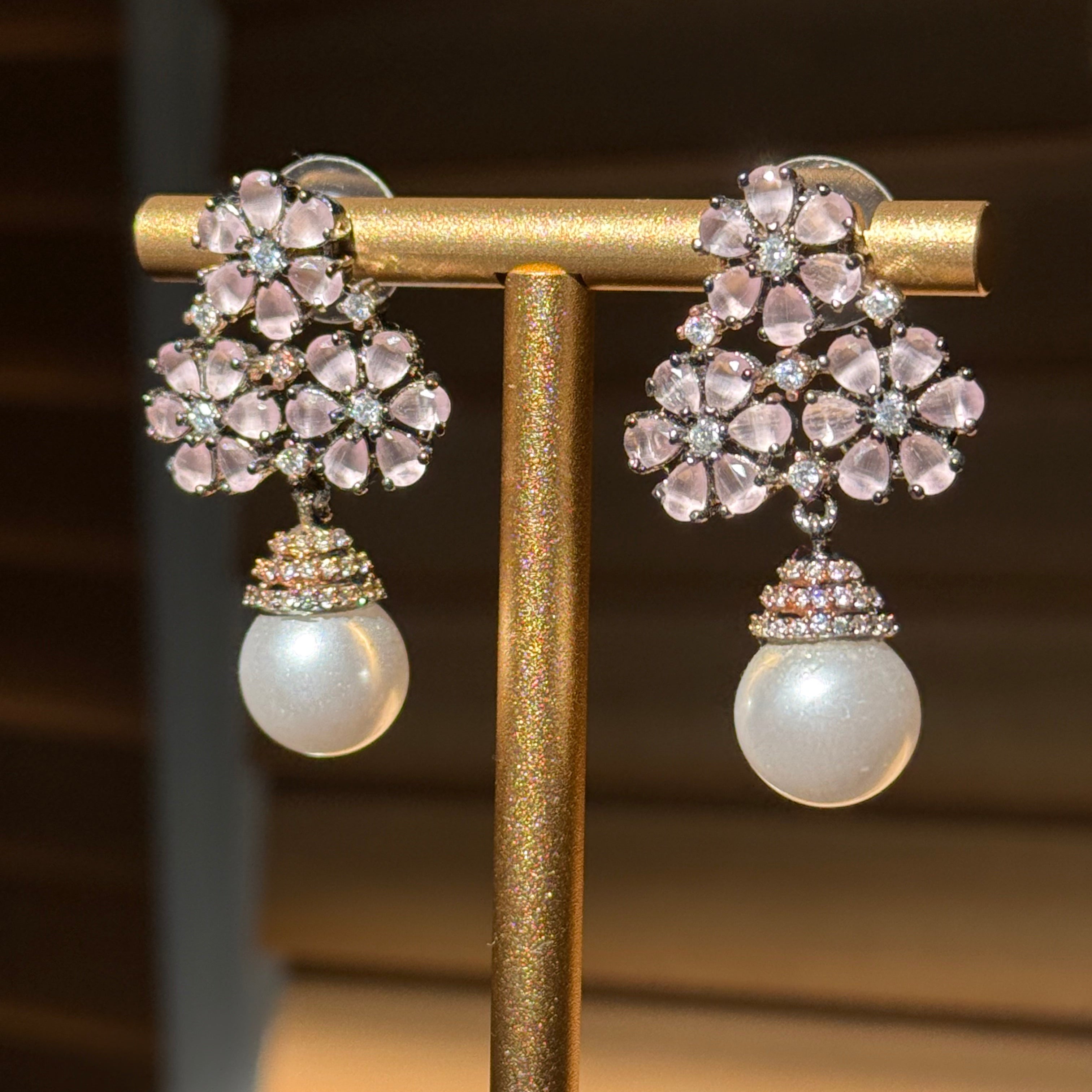 Pair of earrings with floral design and pearl-like elements on a stand.