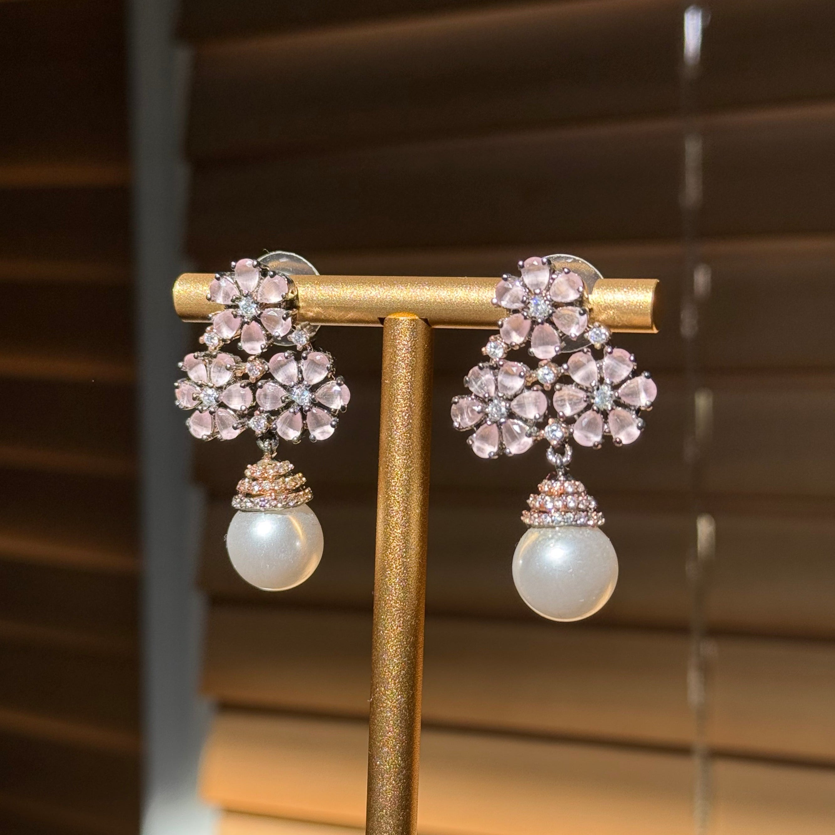 Pair of earrings with floral design and pearl accents on a stand against a blurred background