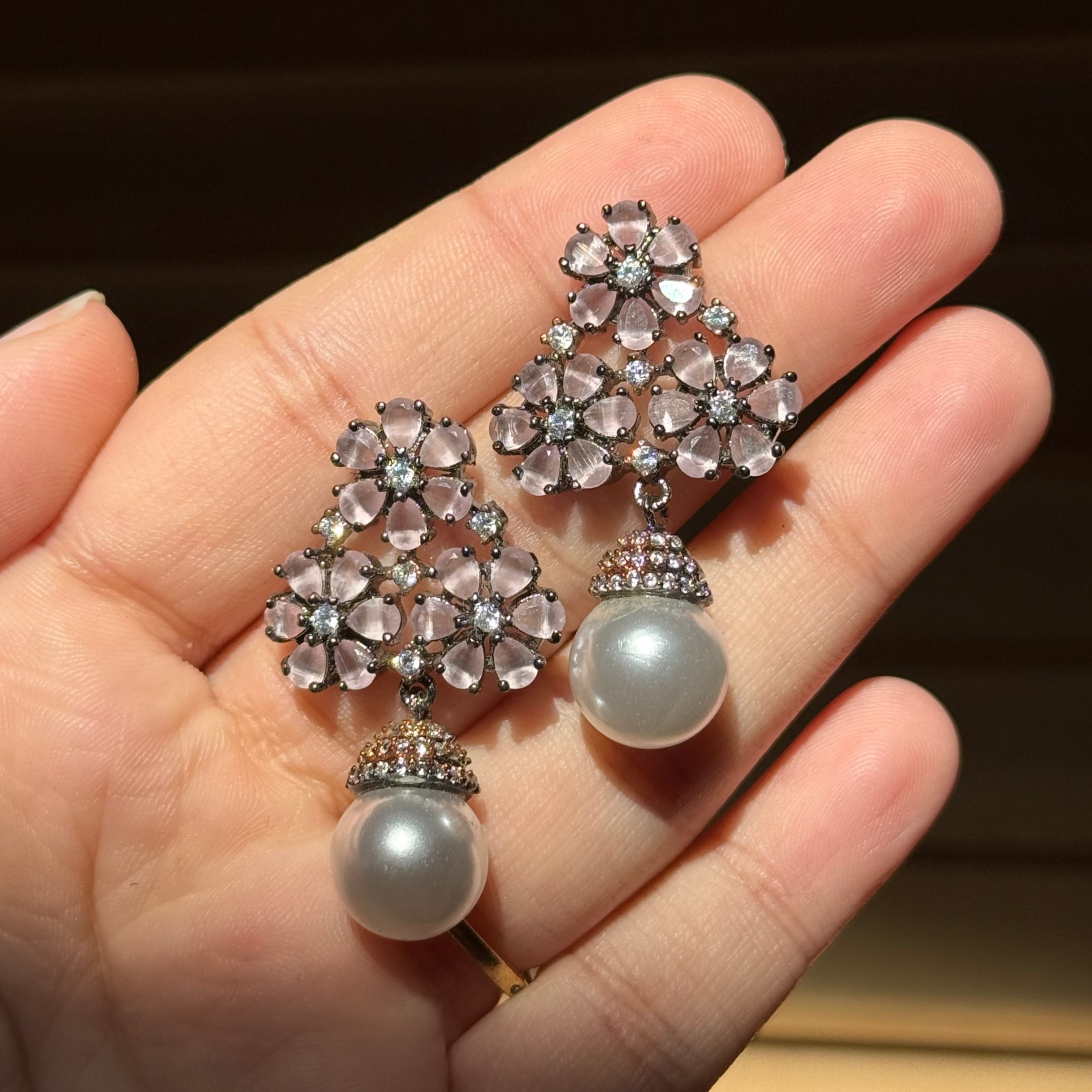 Pair of floral earrings with pearl drops held in a hand against a neutral background