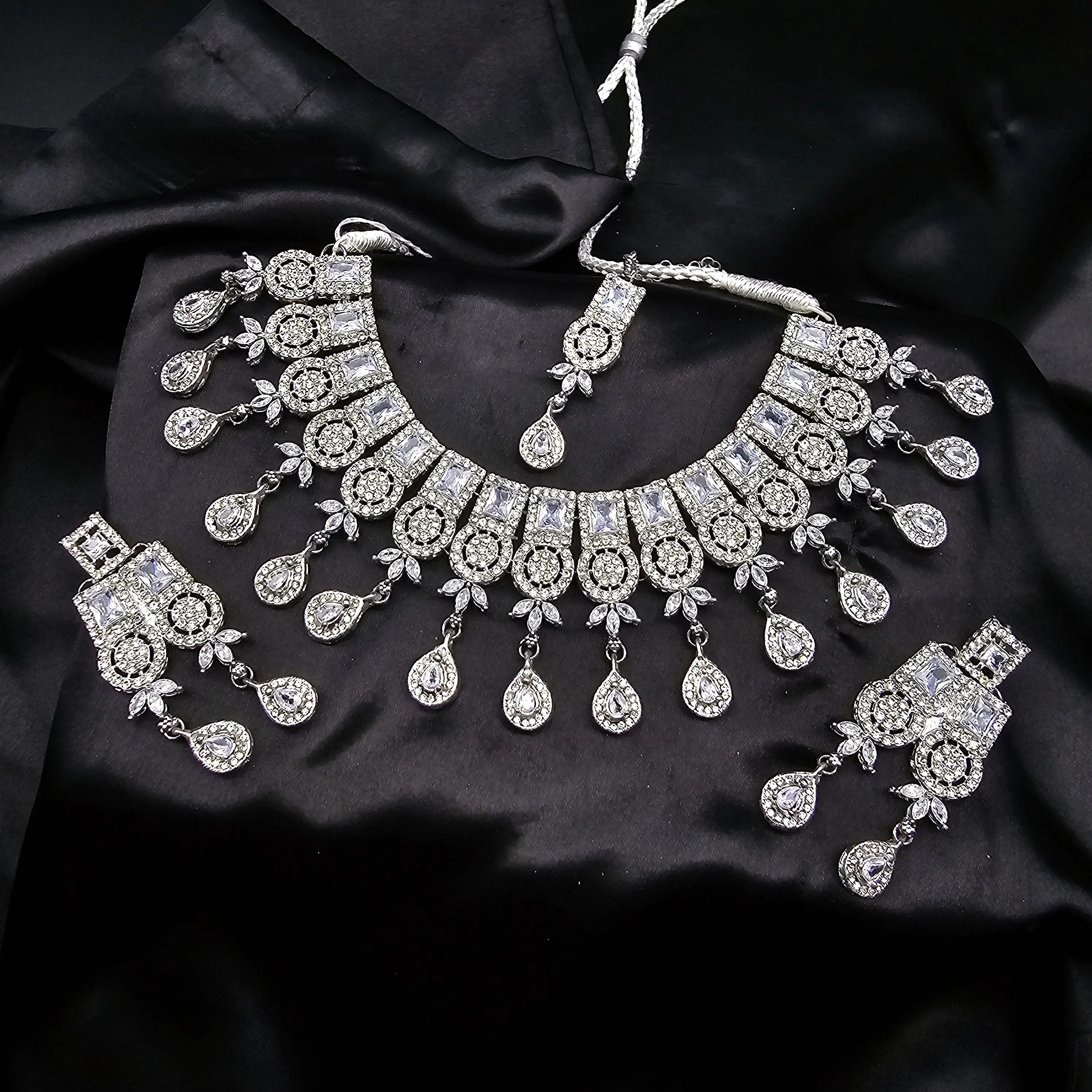 Ishq necklace set in classic silver variant with CZ stones, earrings, and tikka on black satin background.