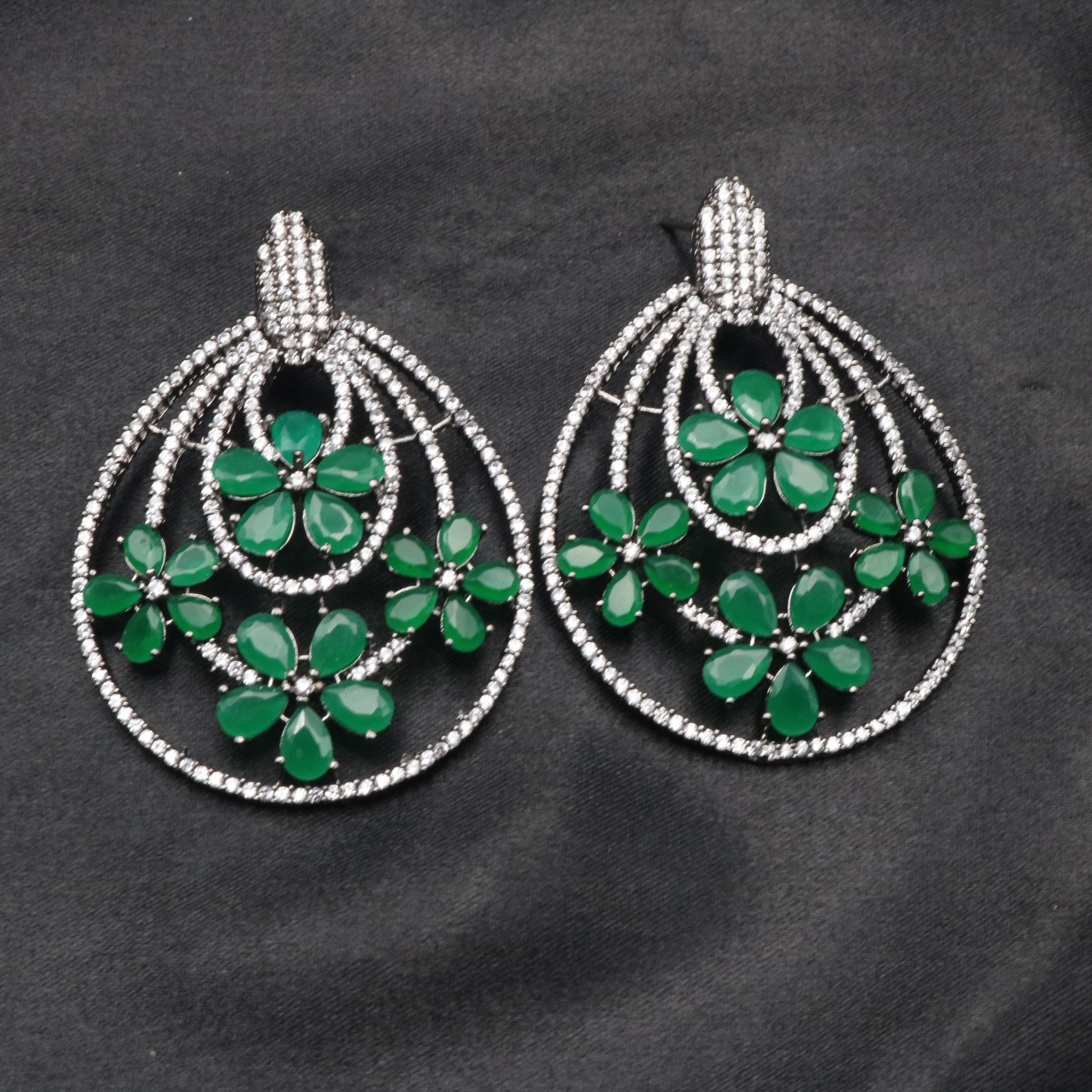 A pair of stainless steel earrings with a floral design, featuring green stones and American diamond accents.