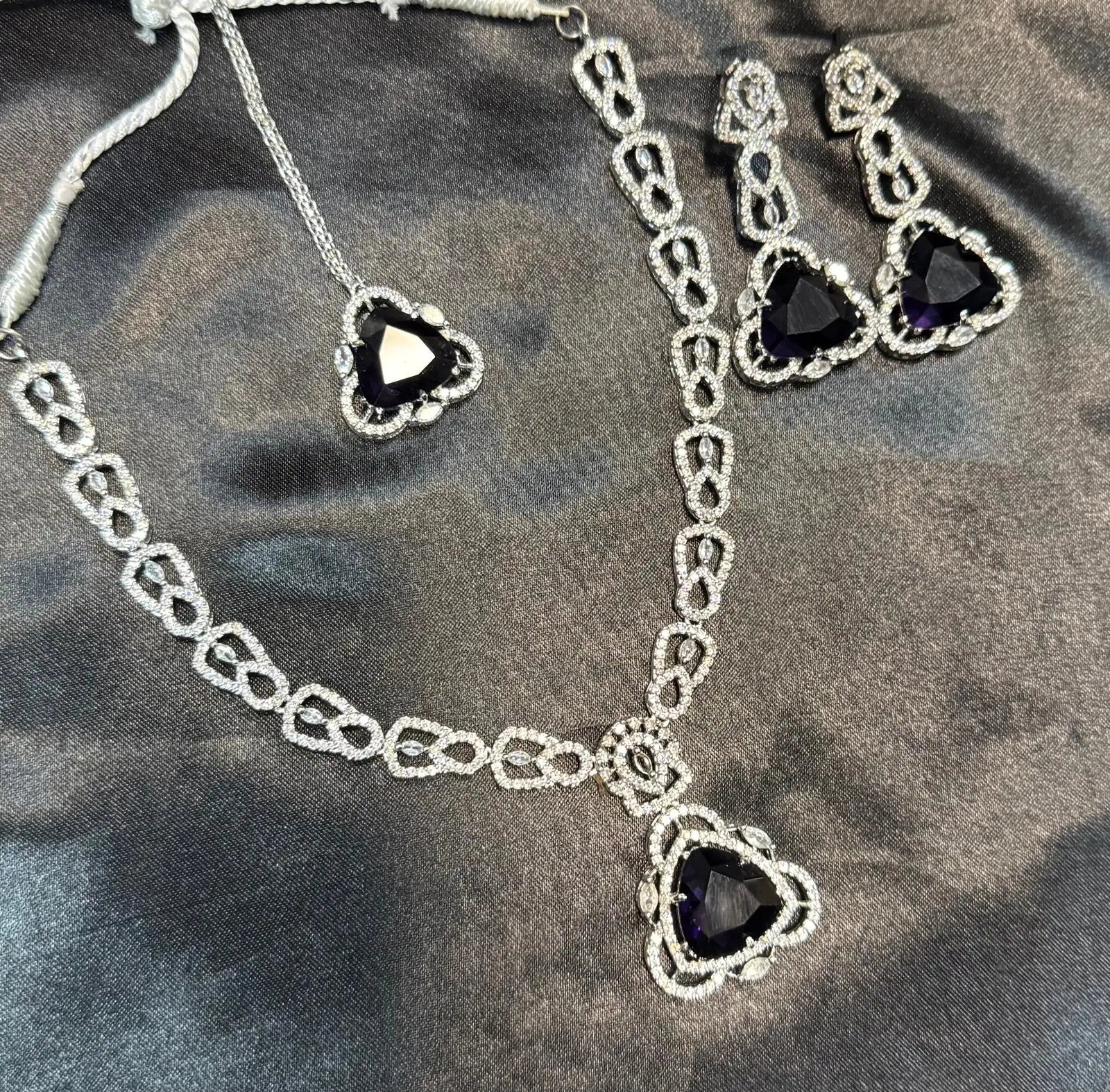 Flat lay of JV158 full necklace set including earrings and maang tikka with heart-shaped violet stones.