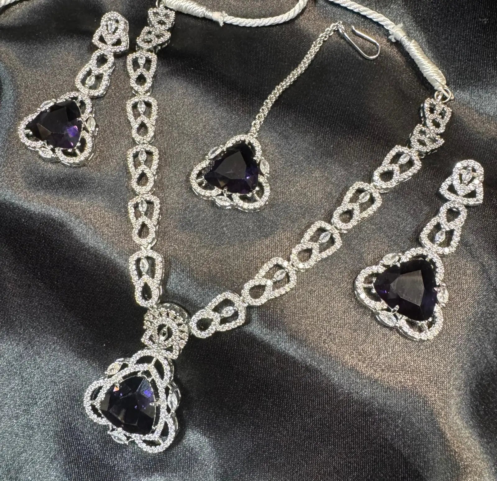 JV158 necklace set on satin background showing full layout of necklace, earrings, and tikka in silver finish.