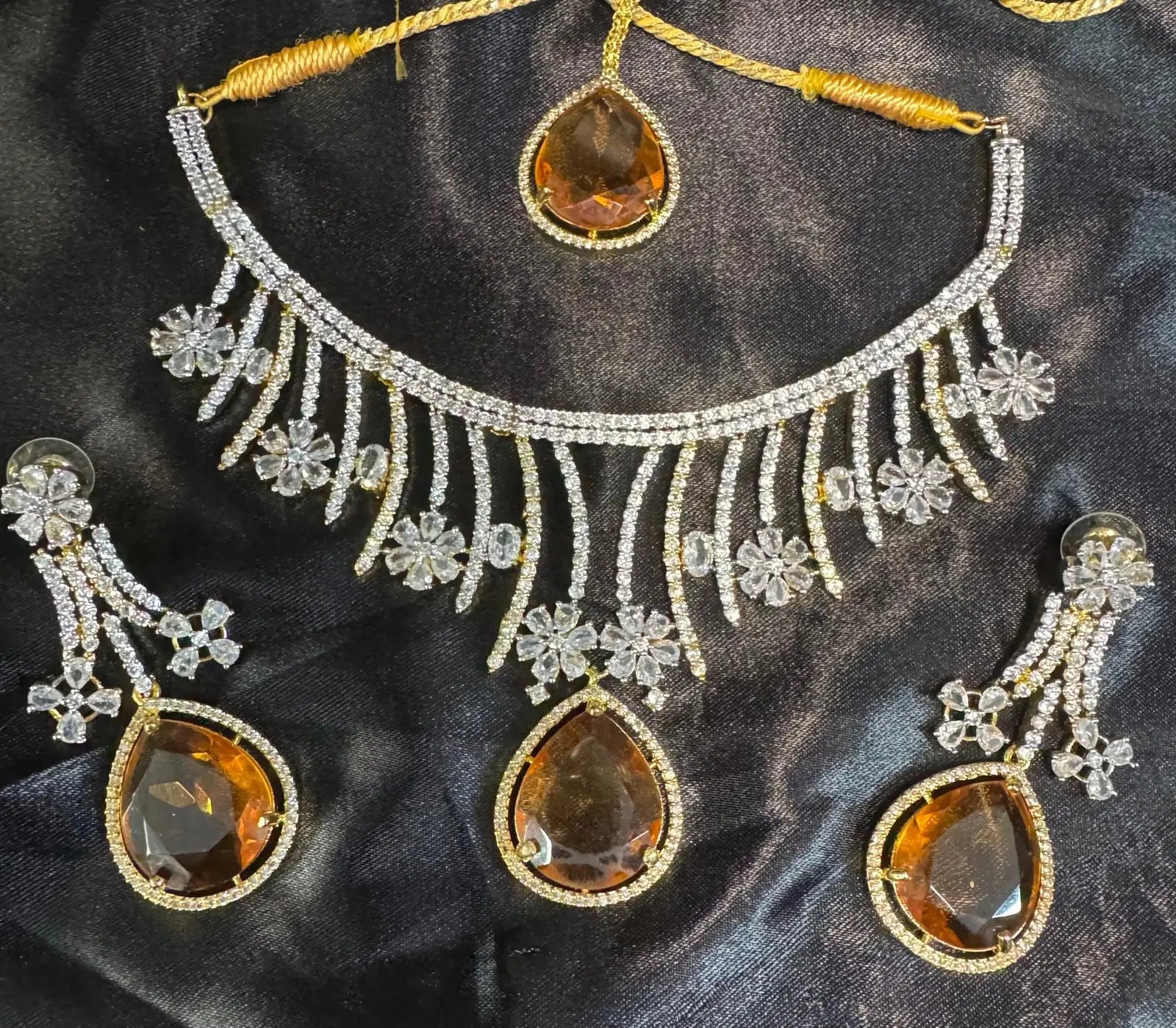 Flat lay of JV159 necklace set showcasing floral CZ work and amber teardrop stones against satin fabric.