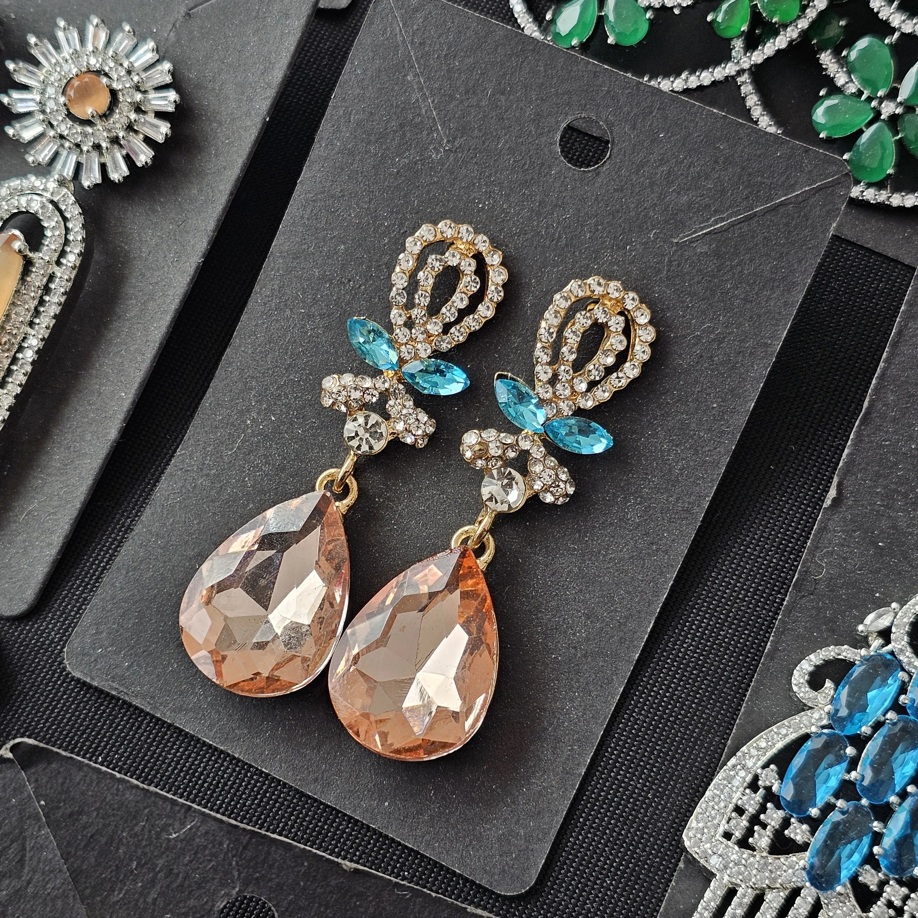 Pair of ornate earrings with teardrop-shaped stones on a black card.