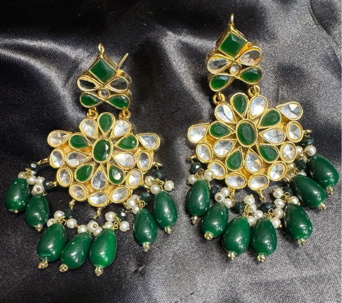 Pair of green and gold earrings on a dark fabric background