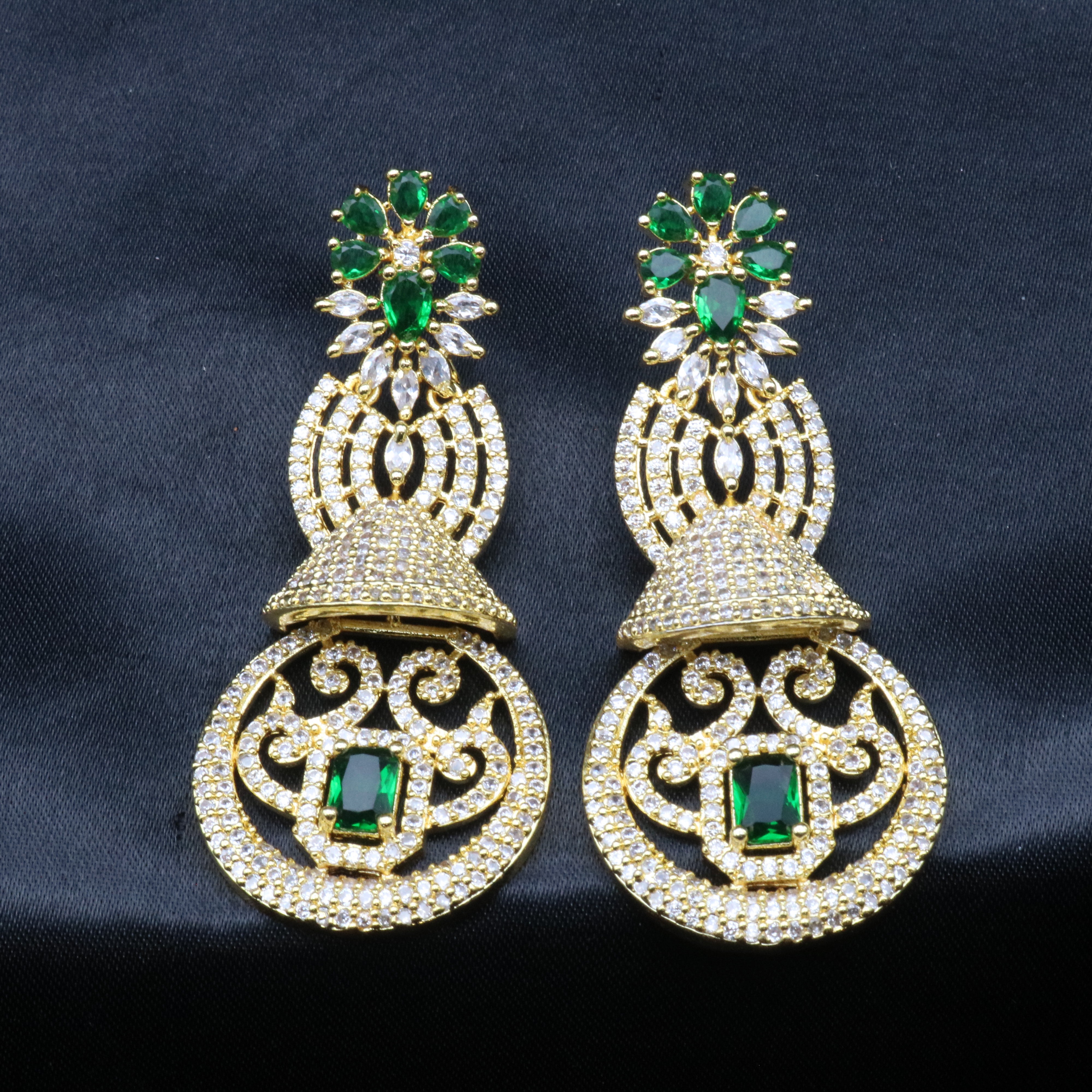 another angle of a pair of gold-toned earrings with green and clear stones set in ornate filigree designs.