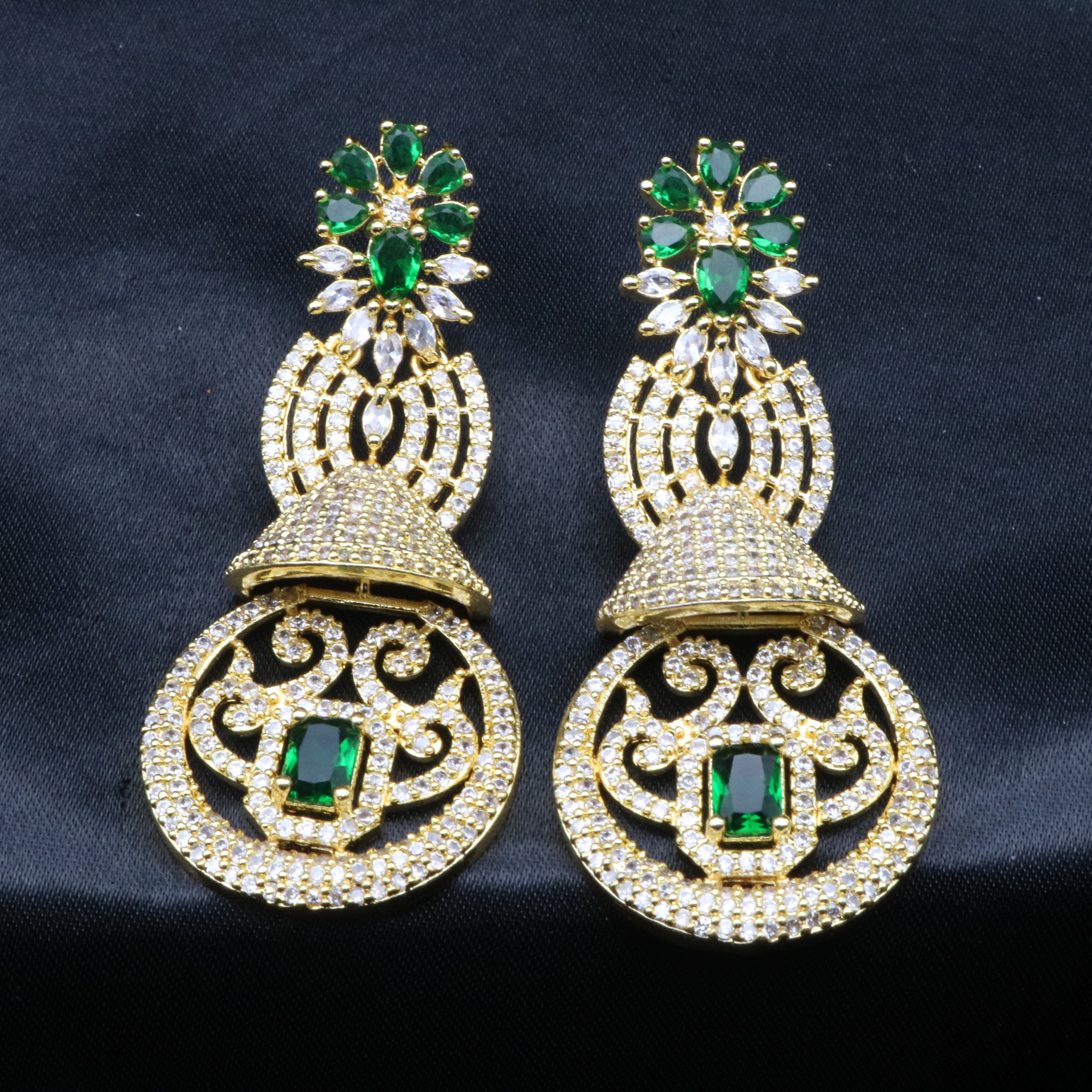 A pair of gold-toned earrings with green and clear stones set in ornate filigree designs.