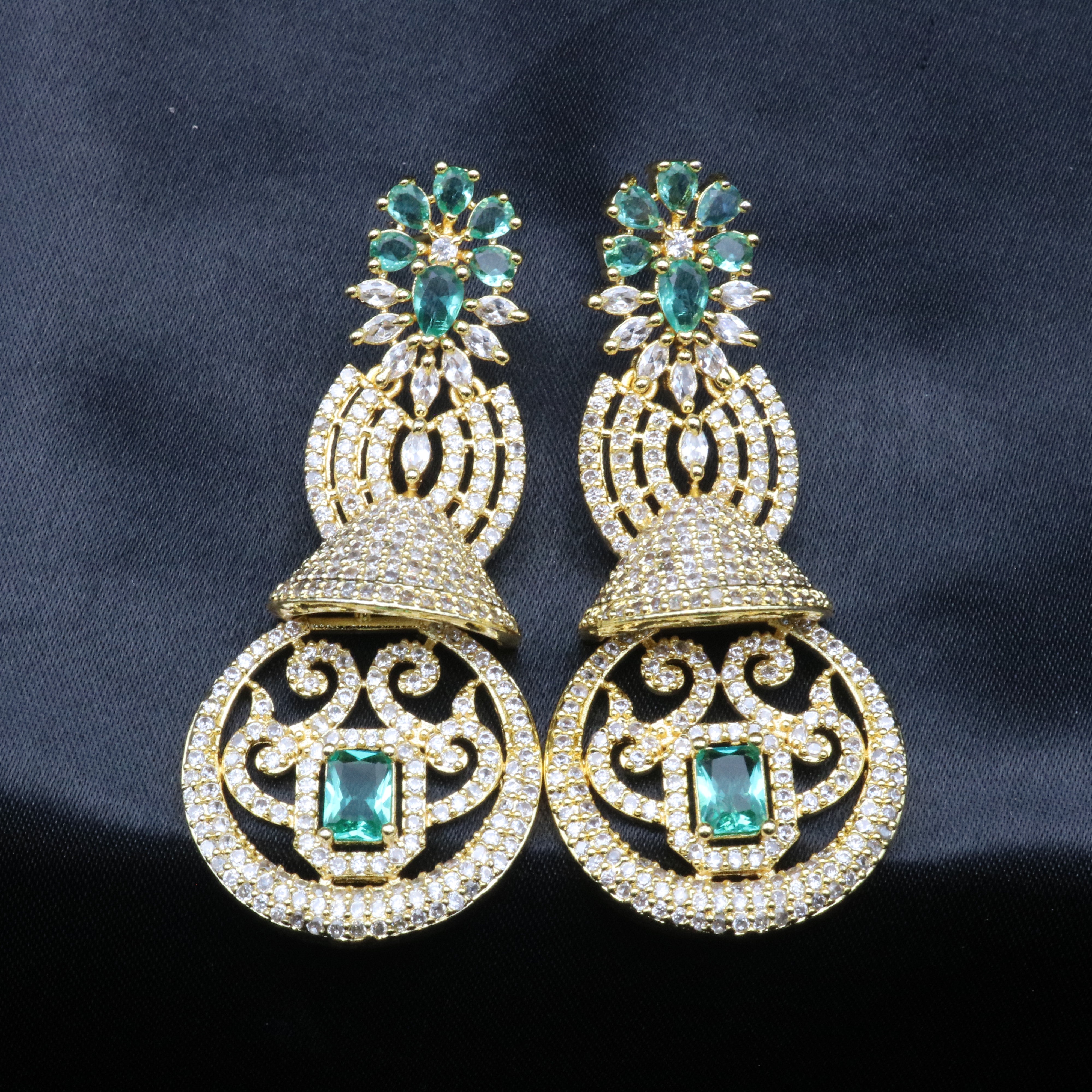 another angle of a pair of gold-toned earrings with sea green and clear stones set in ornate filigree designs.