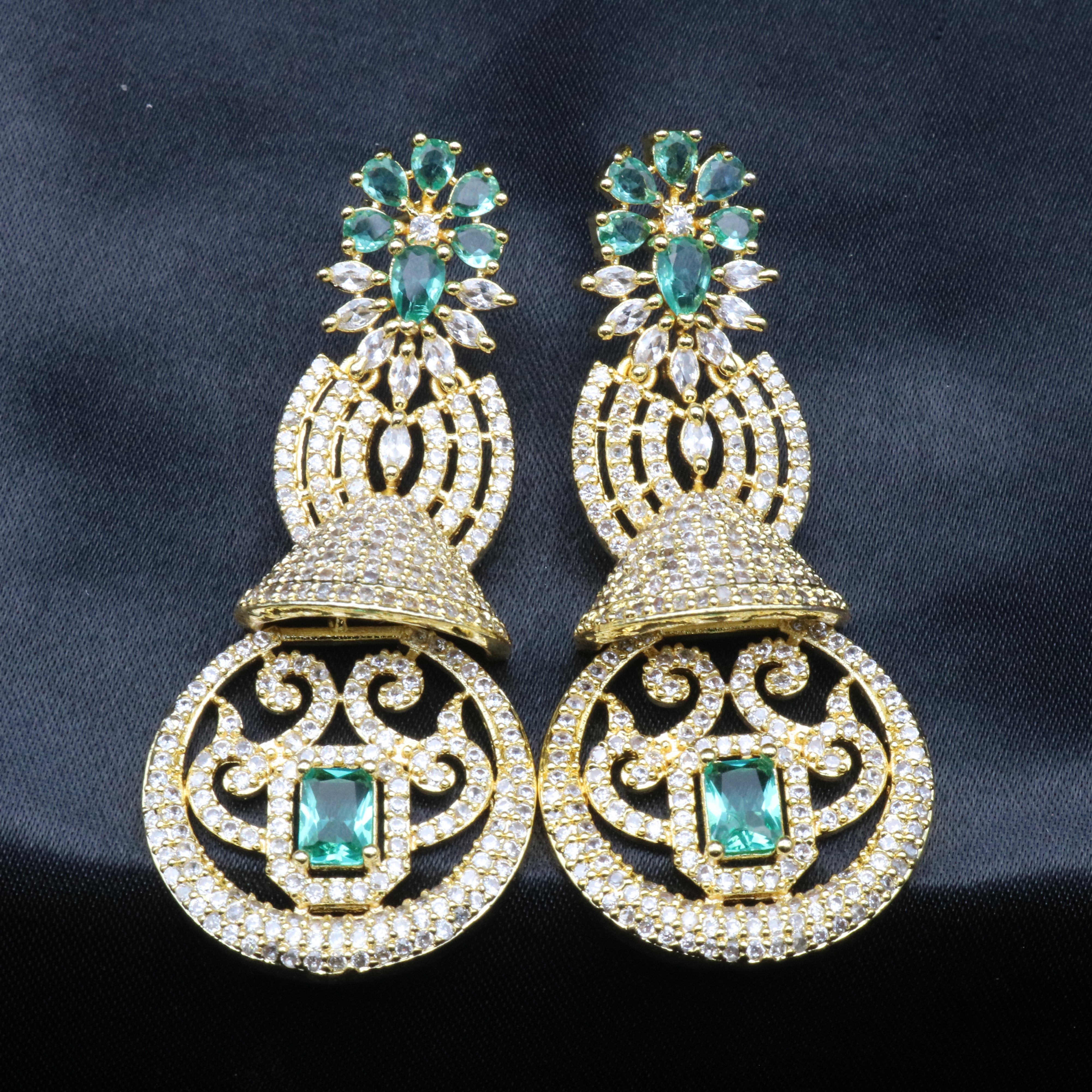 top view of a pair of gold-toned earrings with sea green and clear stones set in ornate filigree designs.