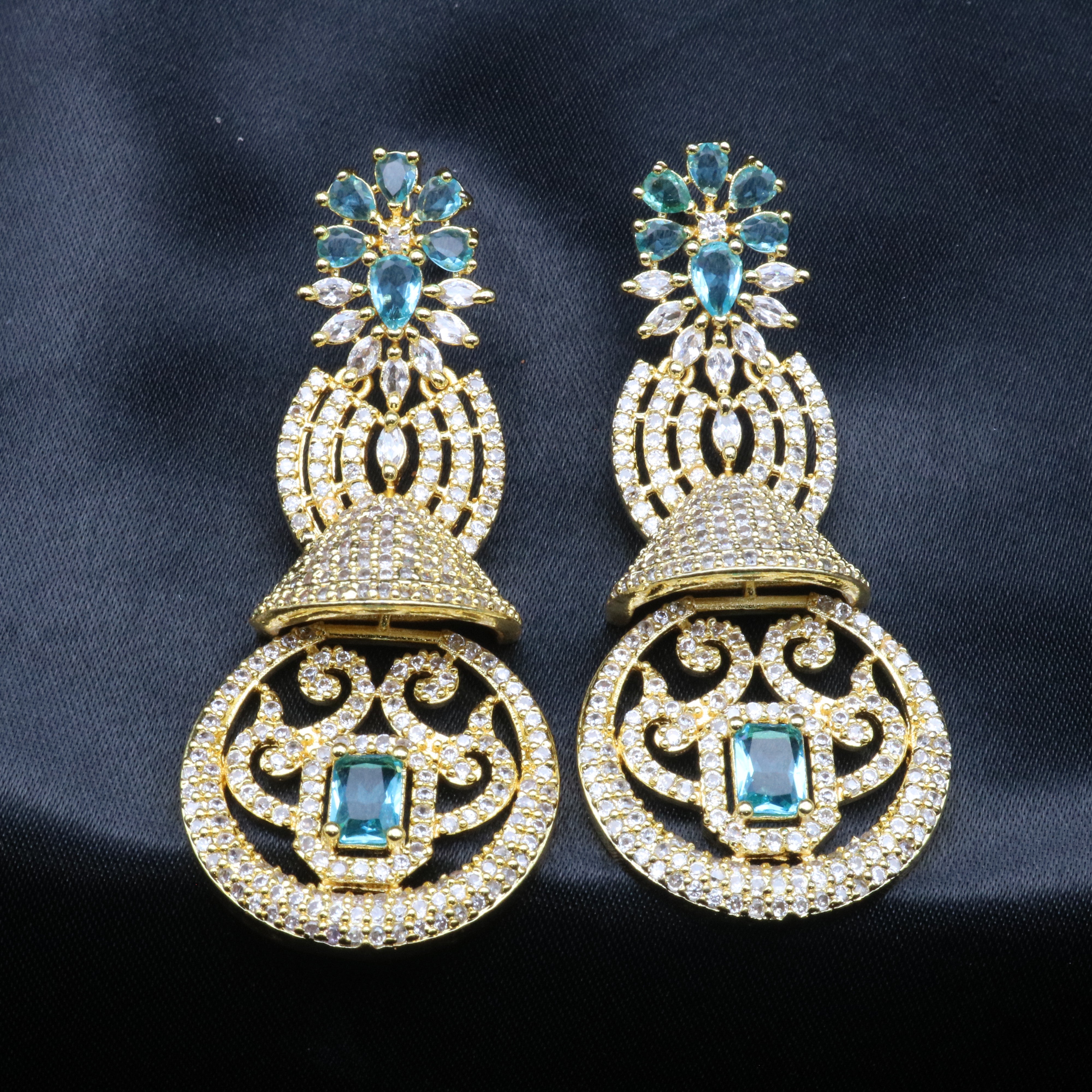 A pair of gold-toned earrings with sea green and clear stones set in ornate filigree designs.