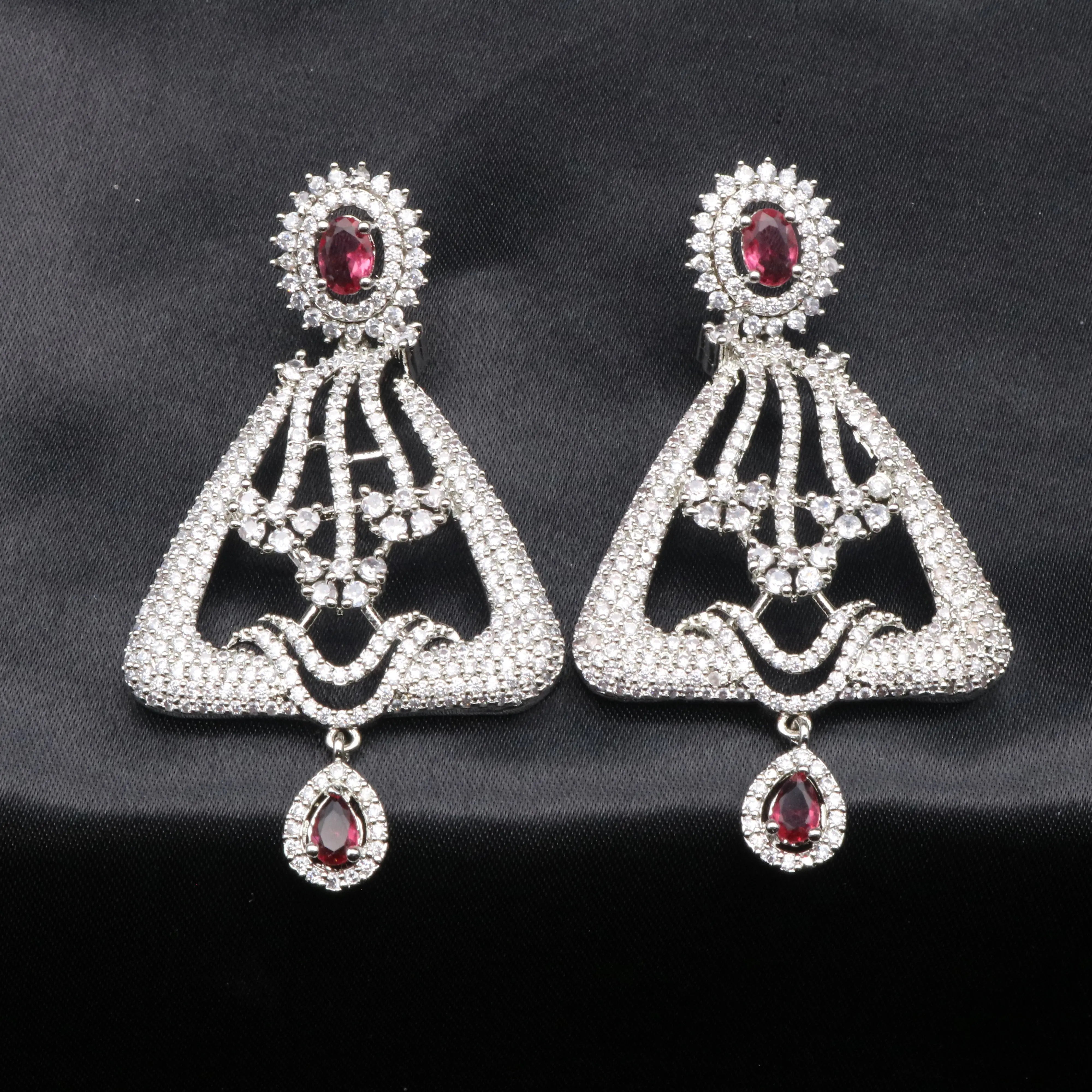 A pair of silver-colored chandelier earrings with red gemstones and intricate detailing, displayed against a black background.