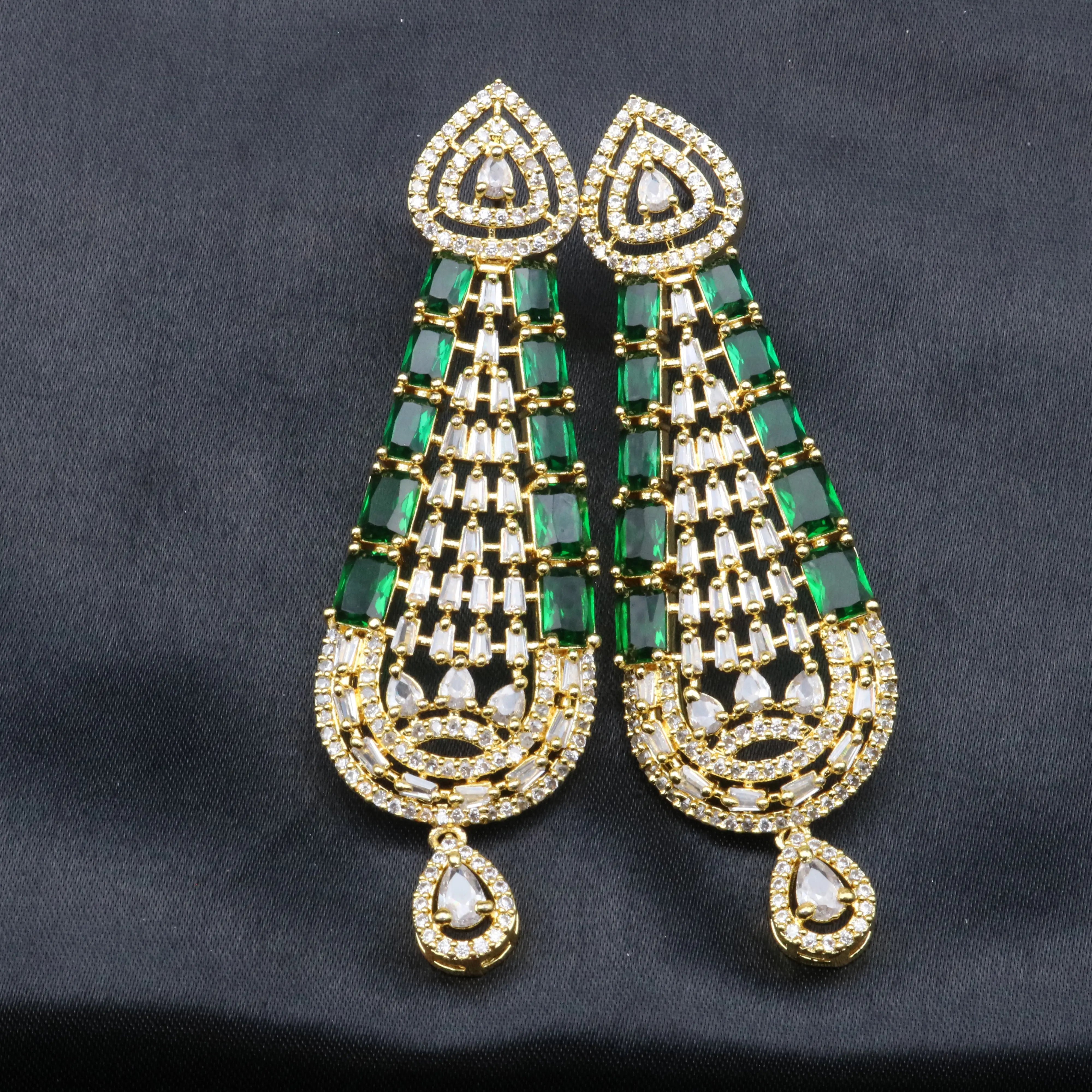 Pair of green and gold American diamonds earrings on a dark background