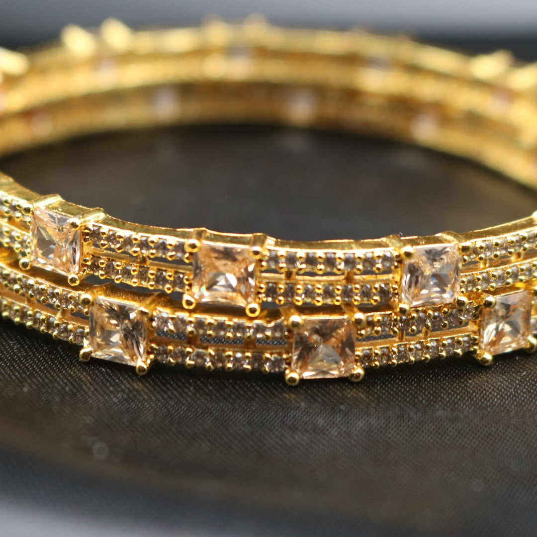 A set of gold-plated bangles adorned with American diamonds, displayed against a dark background.
