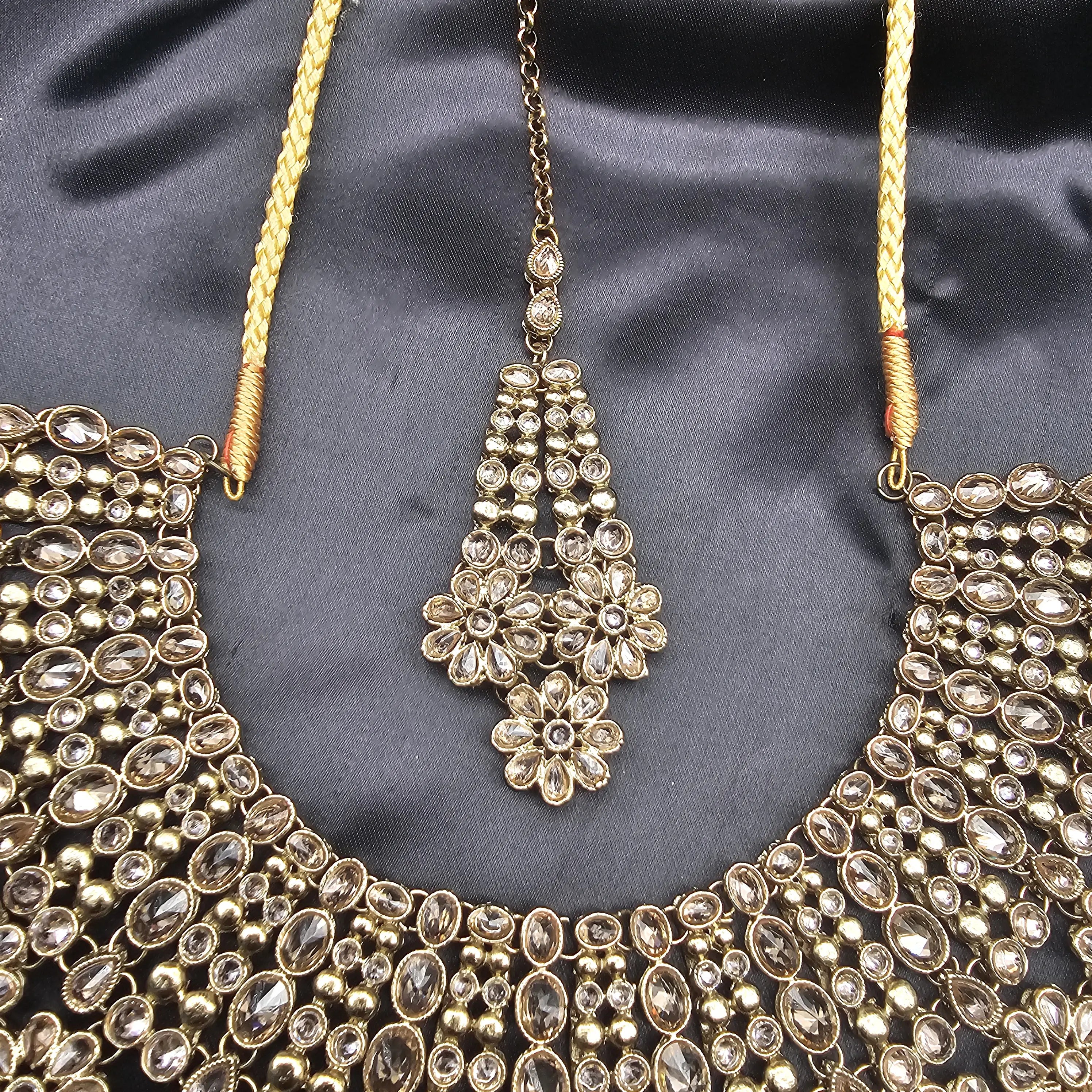 Top view of Magnolia bridal necklace and teeka laid on black fabric background.