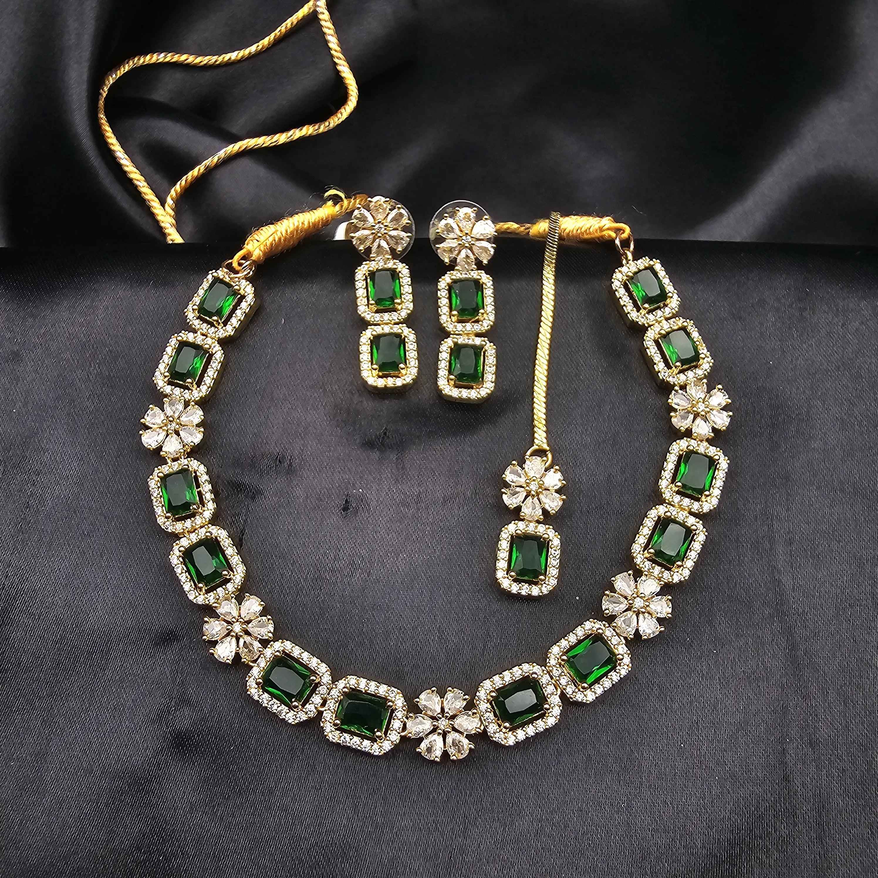Gold-plated necklace set with emerald green rectangular stones and floral CZ motifs displayed on black fabric.