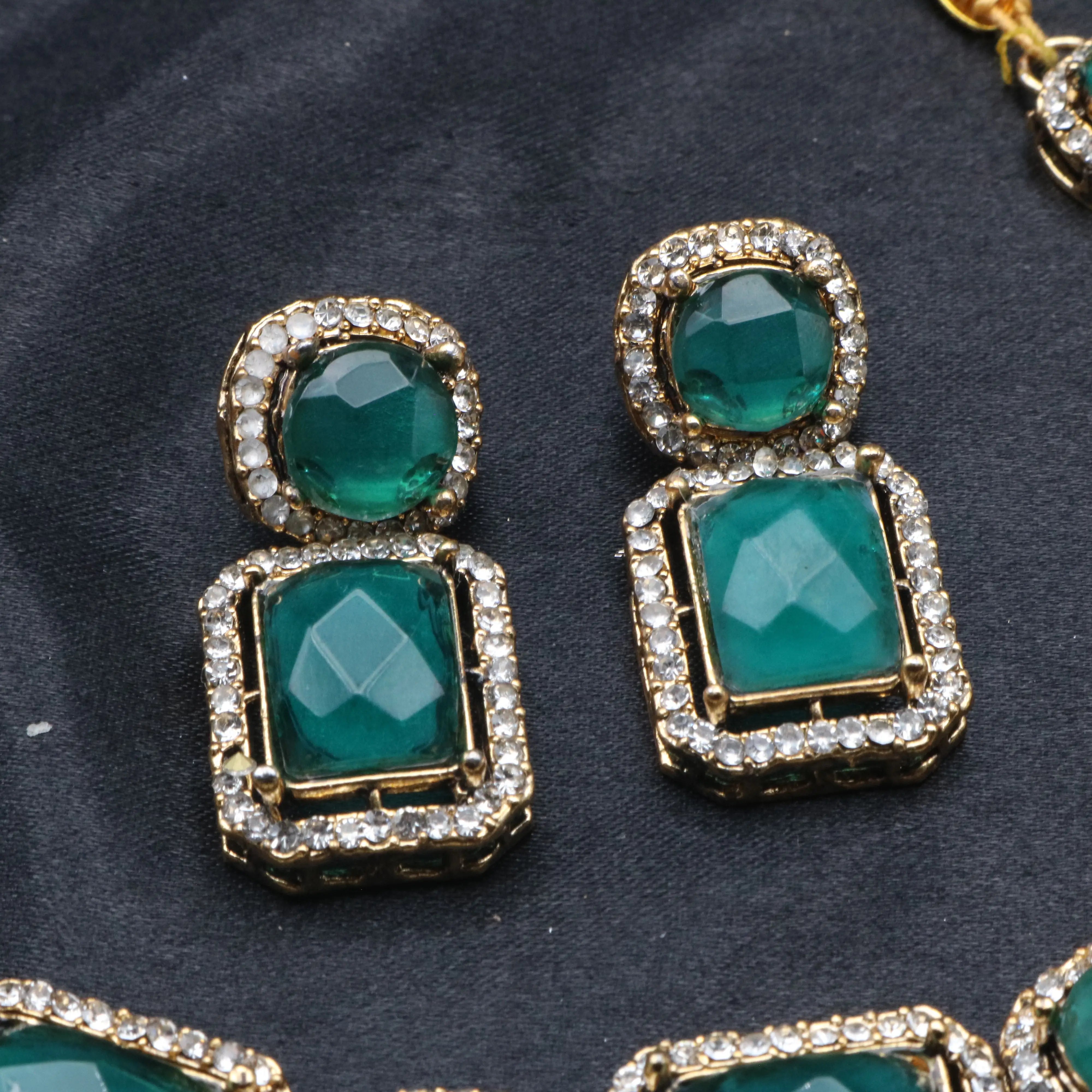 Close-up of Maharaj green earrings featuring round and square stones with gold and diamond border