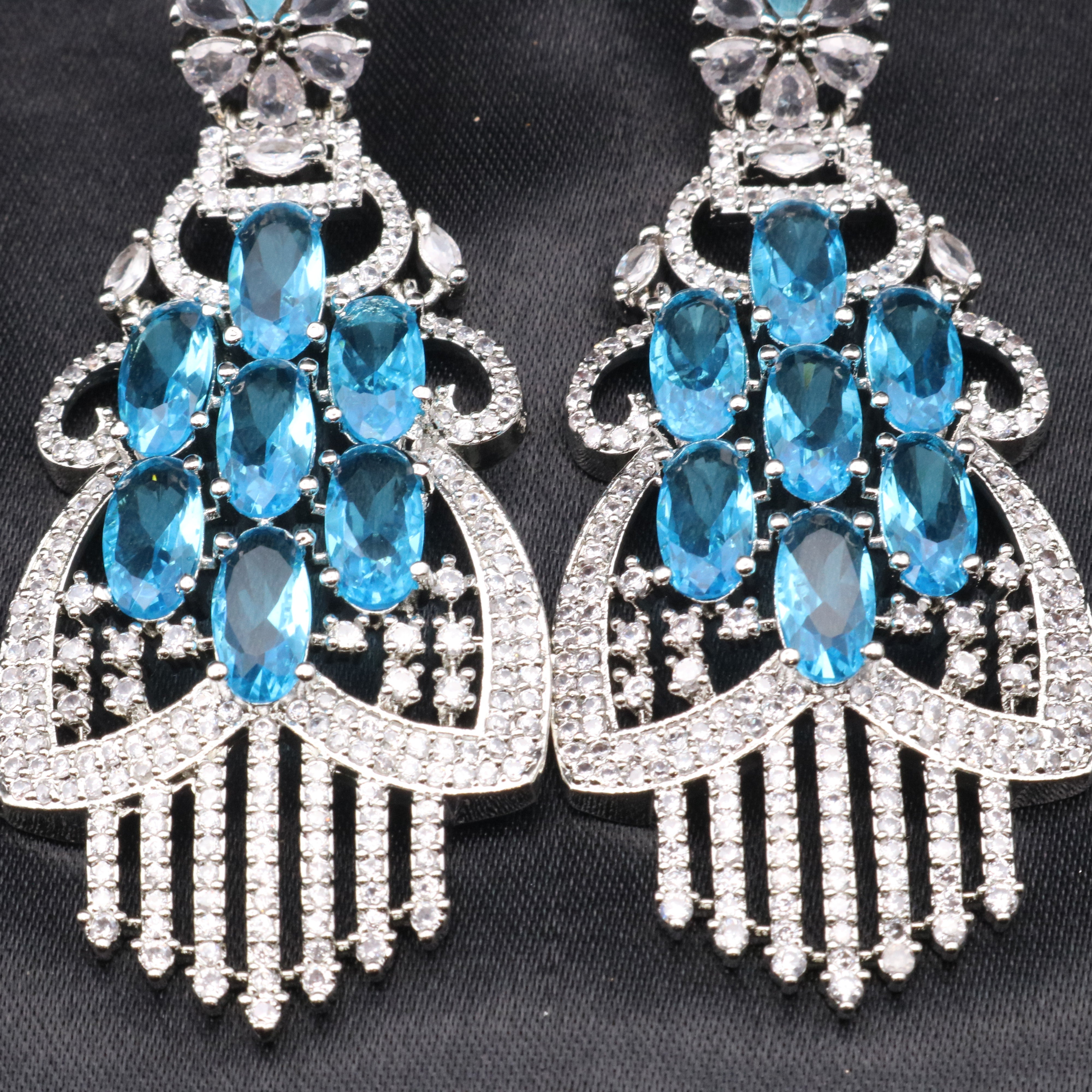 closer view of pair of stainless steel earrings with sparkling blue American diamonds, arranged in a unique geometric pattern, set against a black background.