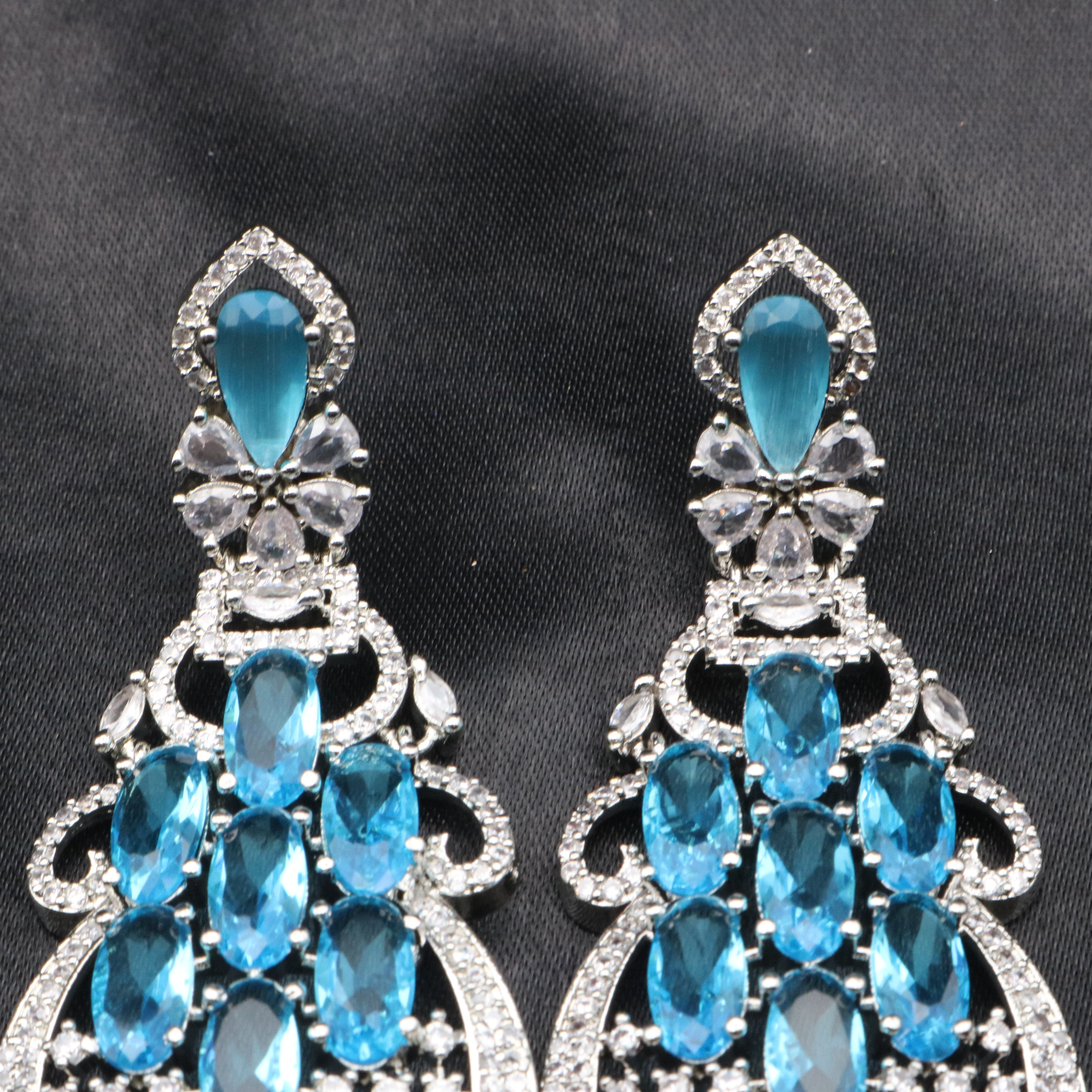 top view of pair of stainless steel earrings with sparkling blue American diamonds, arranged in a unique geometric pattern, set against a black background.