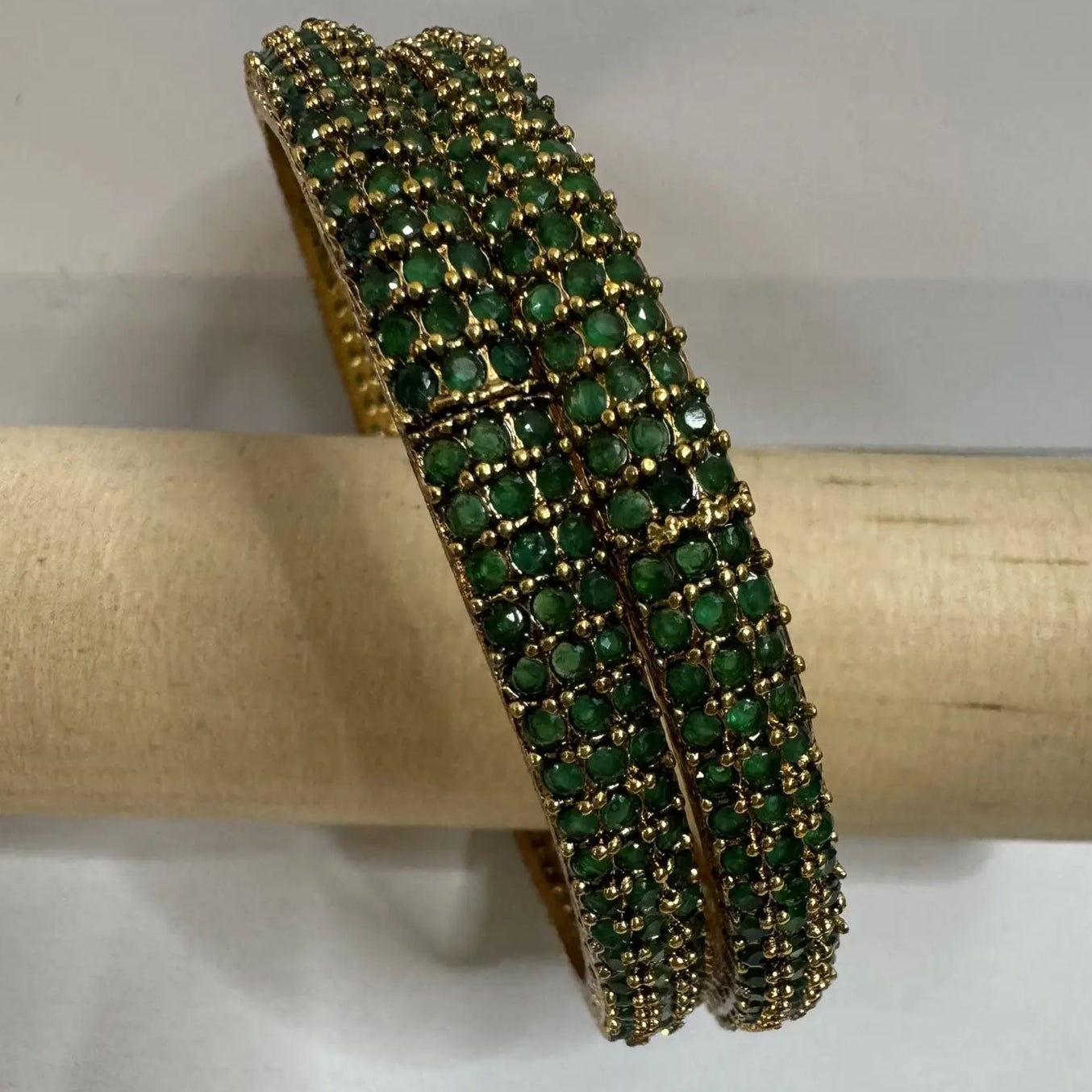 Gold plated bangles with green gemstones on a wooden block with a white background