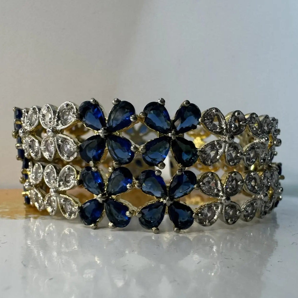 Gold plated bangles with blue and clear gemstones in a floral pattern on a white surface