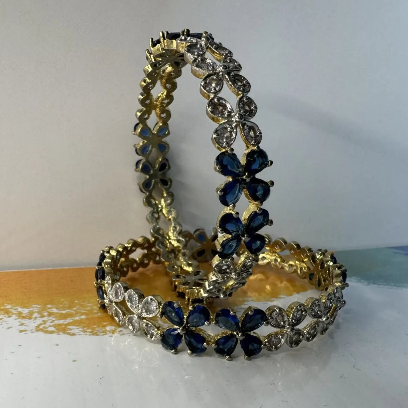 Two gold and blue beaded bangles on a white surface with a blurred background