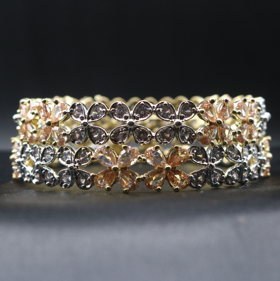 Gold plated bangles with champagne and clear gemstones in a floral pattern and gold accent on a dark surface