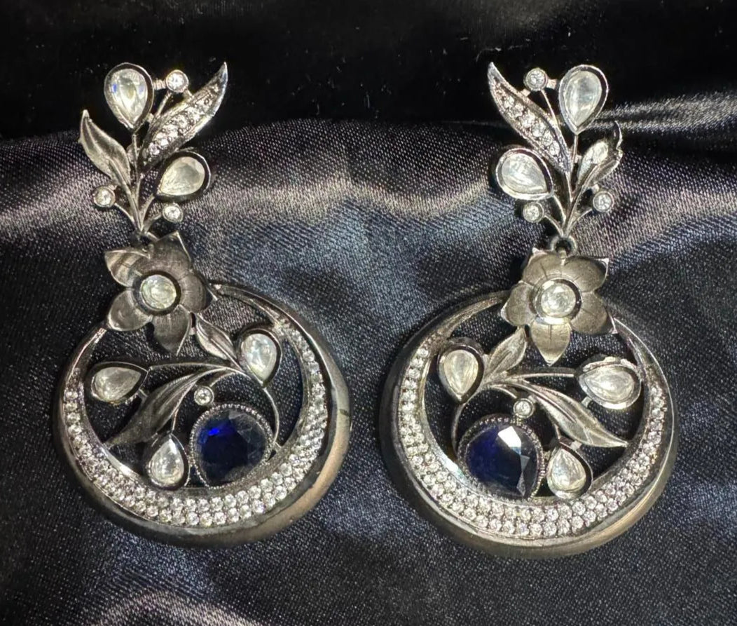 Pair of silver earrings with floral designs on a dark fabric background