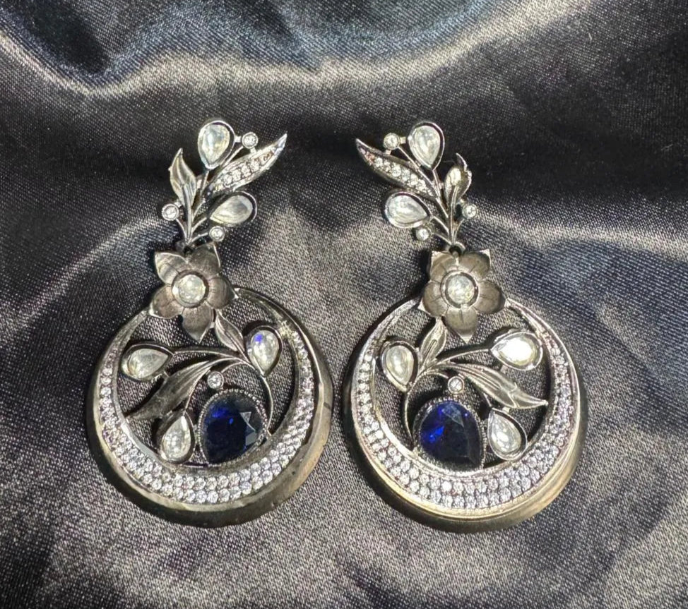 Pair of silver earrings with gemstones and American diamonds on a dark fabric background