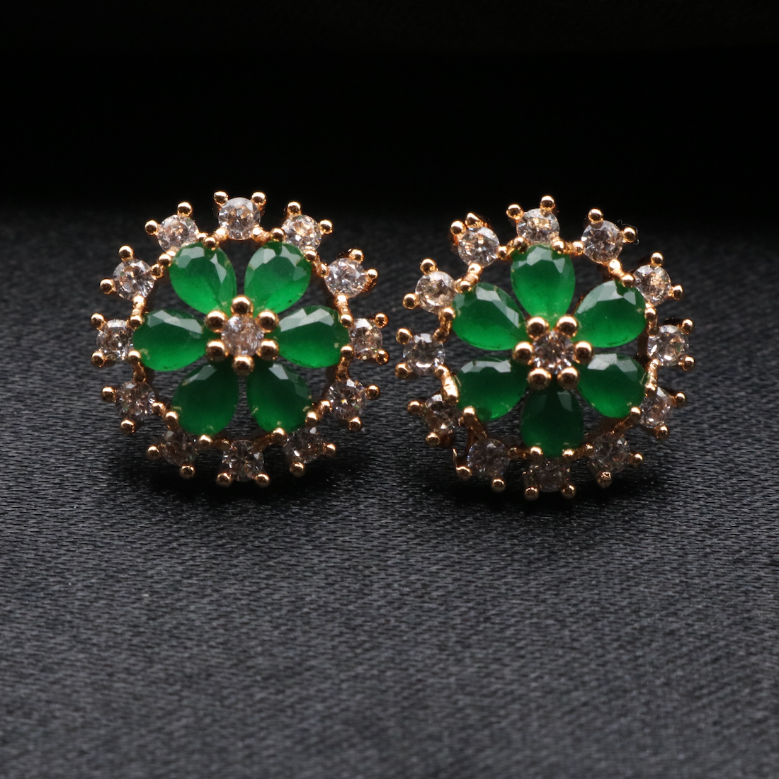 A pair of earrings featuring green gemstones surrounded by gold plating and small clear crystals, part of the PARIS collection.