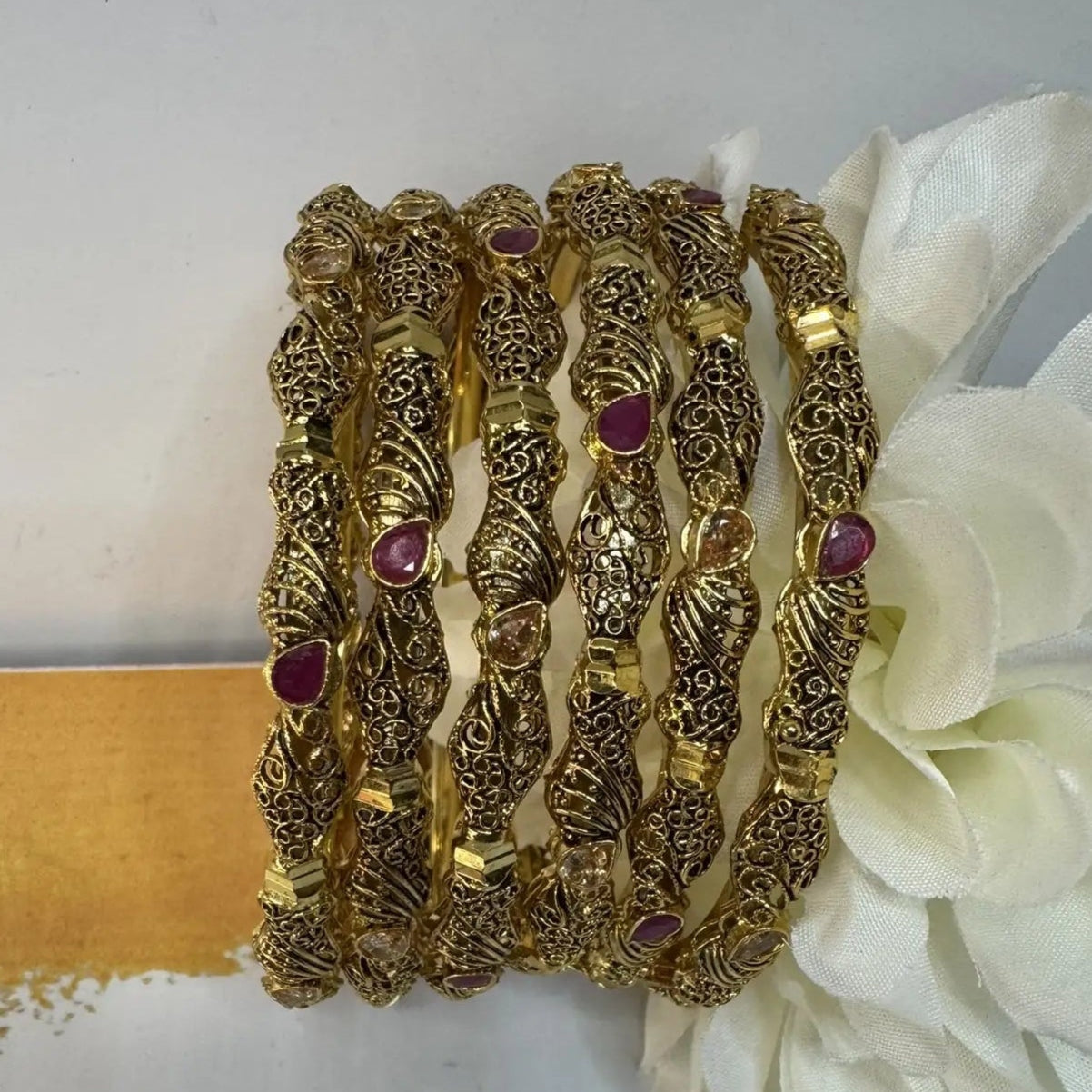 gold-plated bangles with red and champagne embellishments in an upright position on a white surface