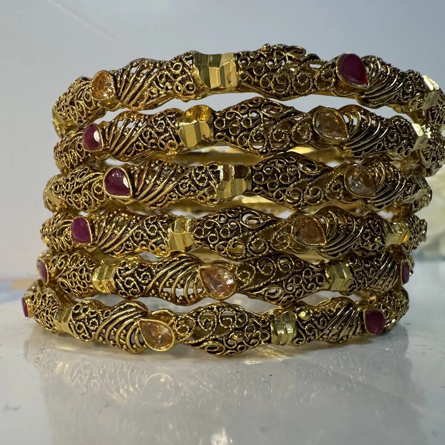 gold-plated bangles with red and champagne embellishments on a white surface
