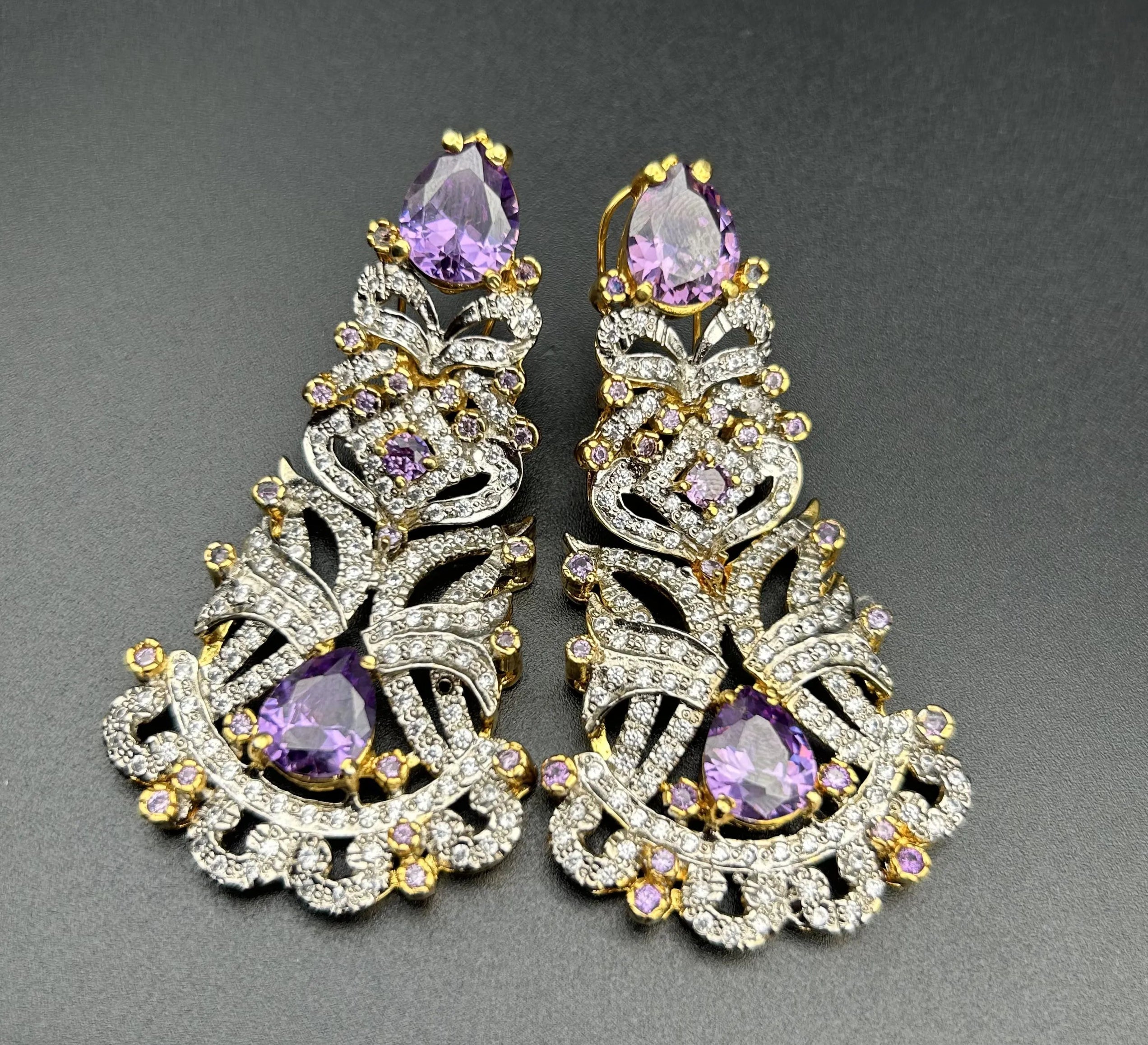 Pair of ornate earrings with purple gemstones on a gray background