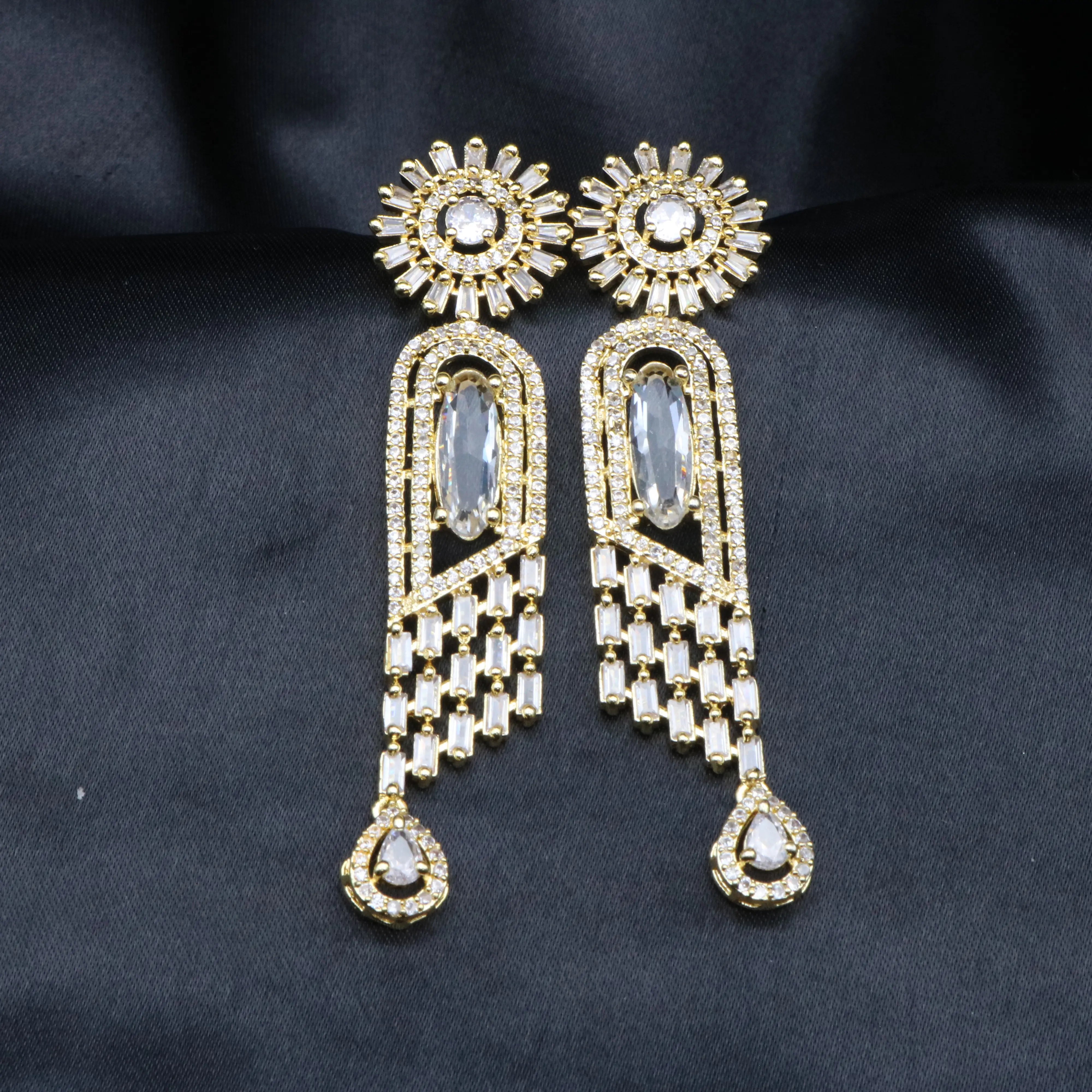 A pair of stainless steel earrings featuring American Diamond accents and a clear gemstone, with a intricate geometric design.