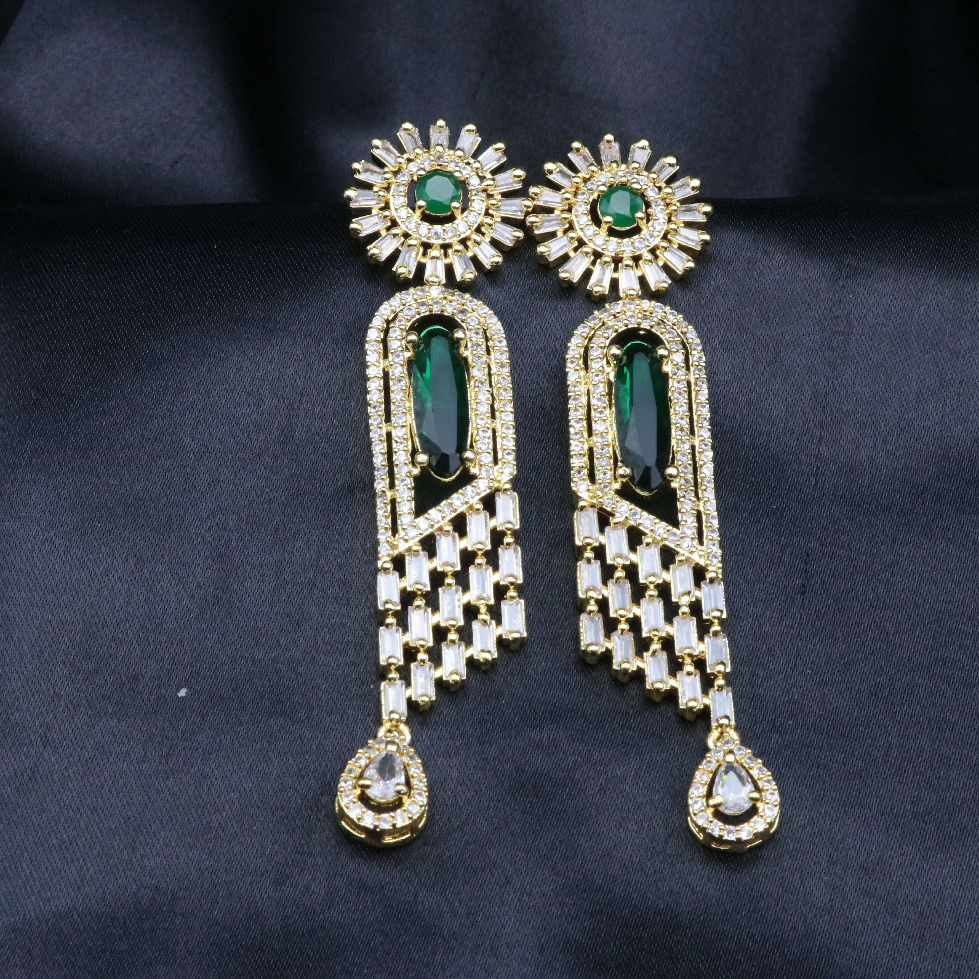 A pair of stainless steel earrings featuring American Diamond accents and a green gemstones, with a intricate geometric design.