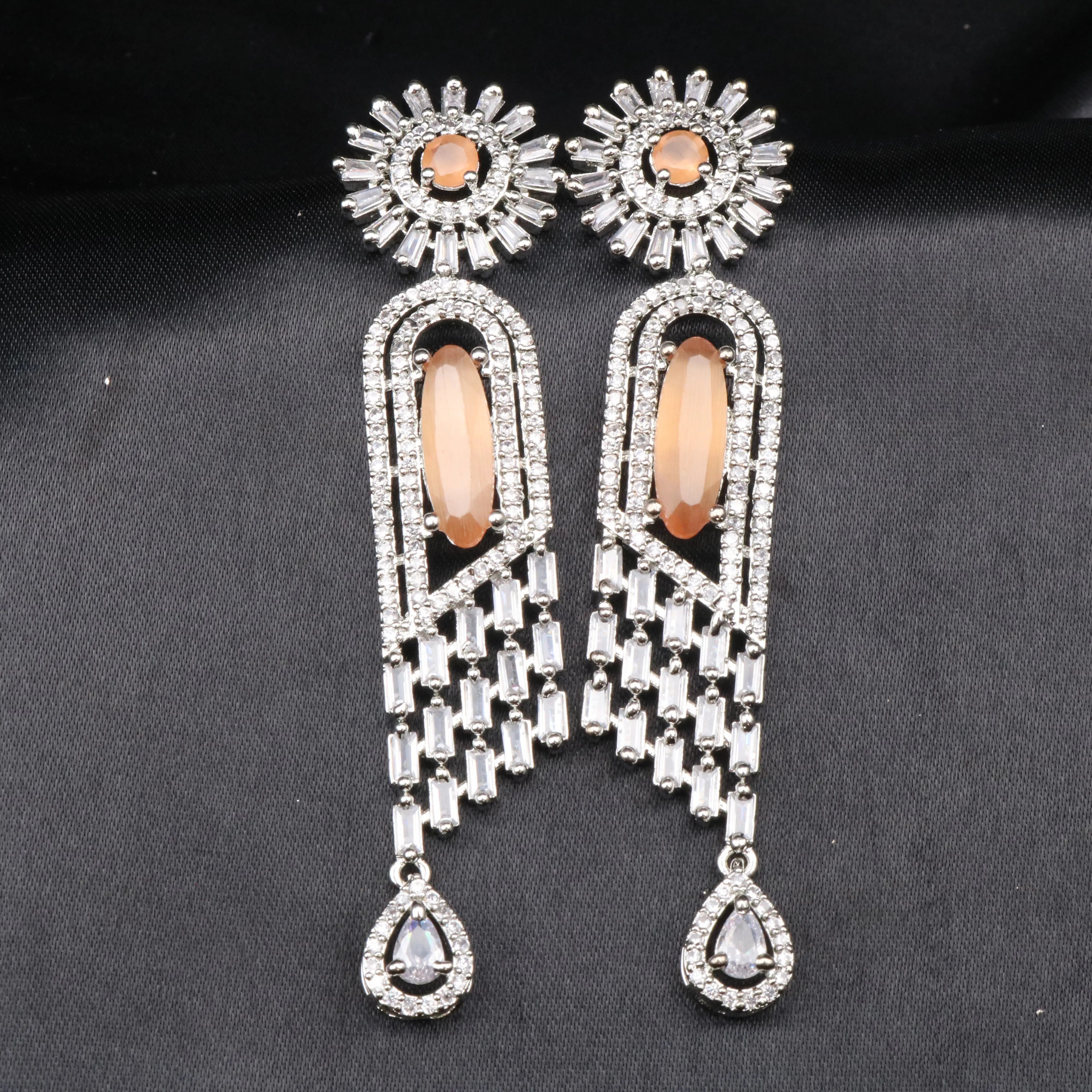 A pair of stainless steel earrings featuring American Diamond accents and a orange gemstones, with a intricate geometric design.