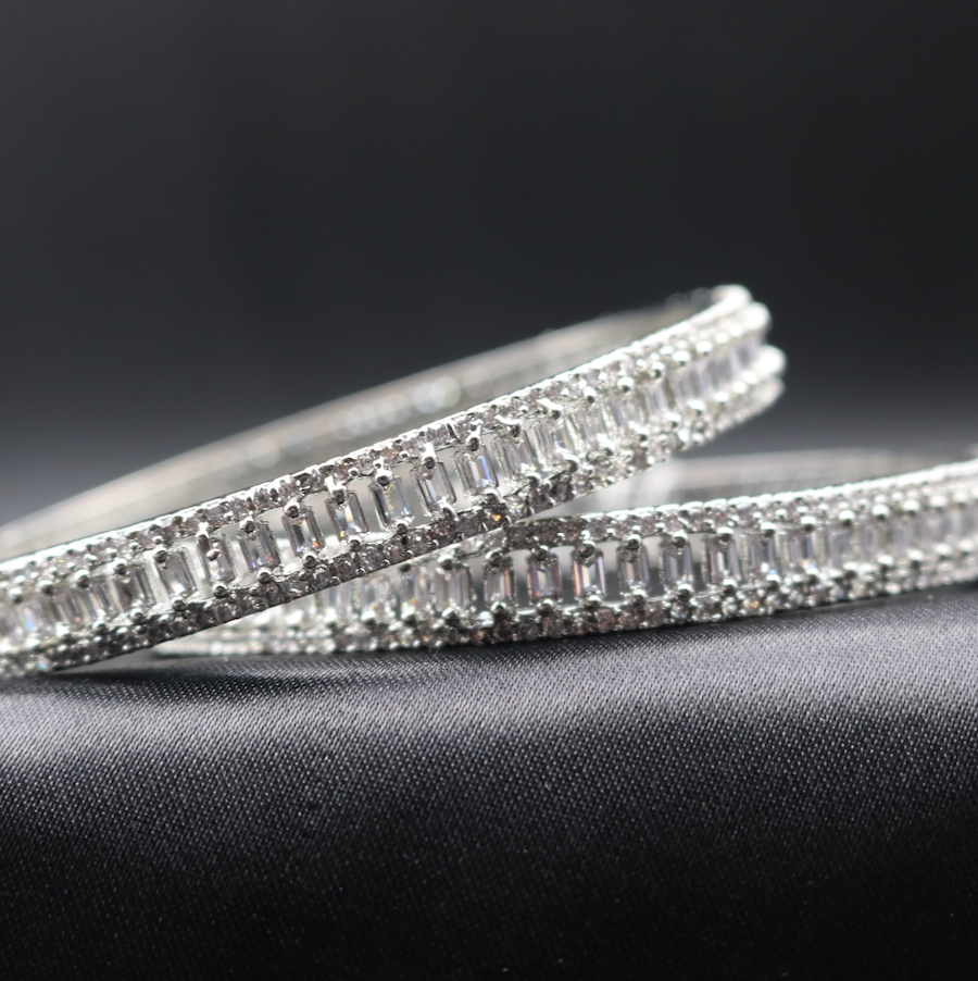 Two stainless steel bangles with American diamond accents on a dark, likely black, textured background.