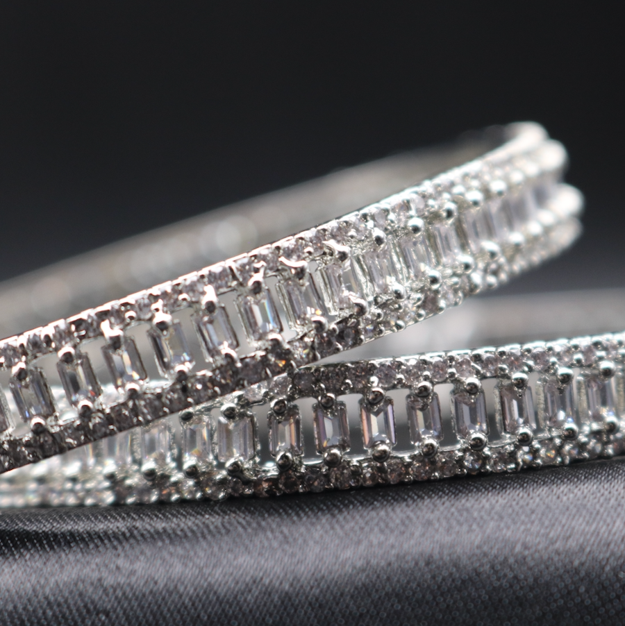 A close-up of two stainless steel bangles with American diamond accents on a dark, likely black, textured background.