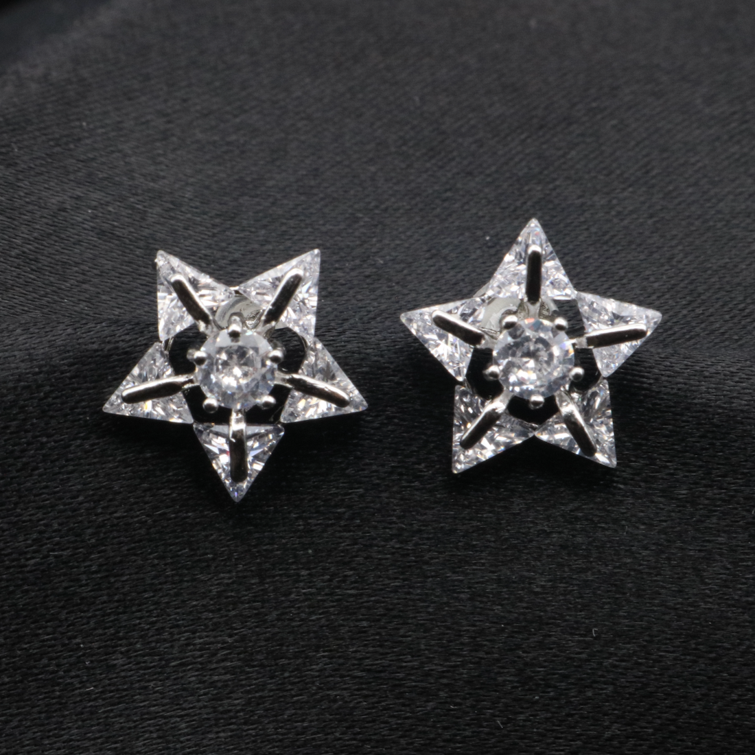 A pair of star-shaped earrings with gold plating and embedded with American diamonds, displayed against a black background.