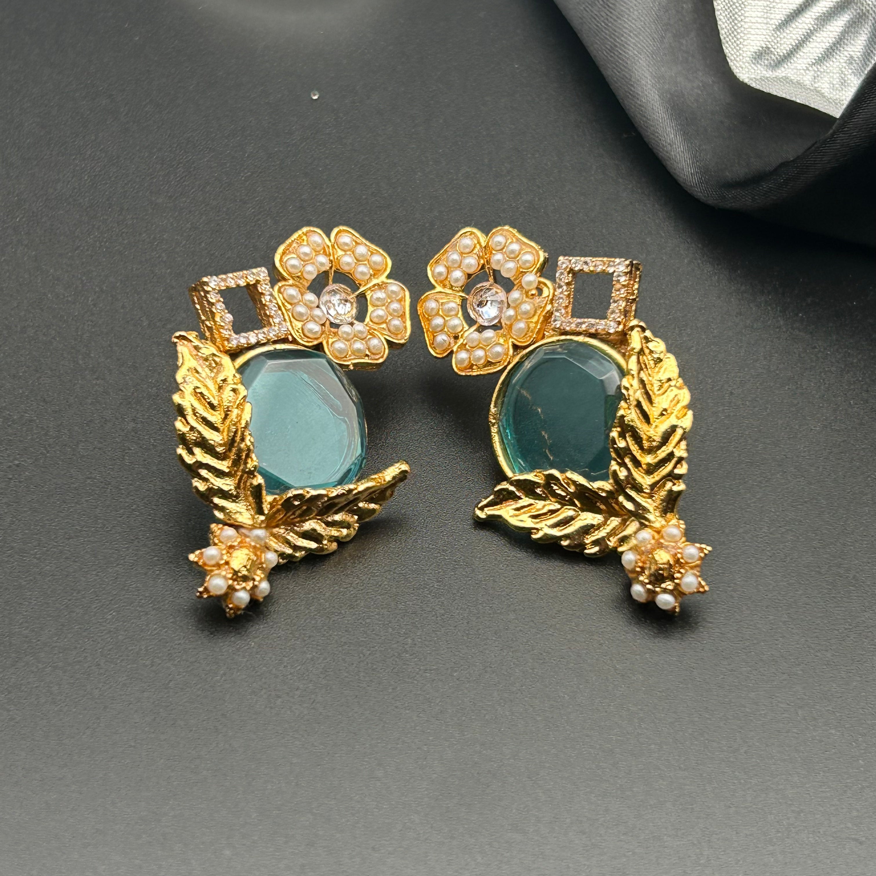 A pair of gold-colored, floral-shaped earrings with blue color tints and gold plated designs.