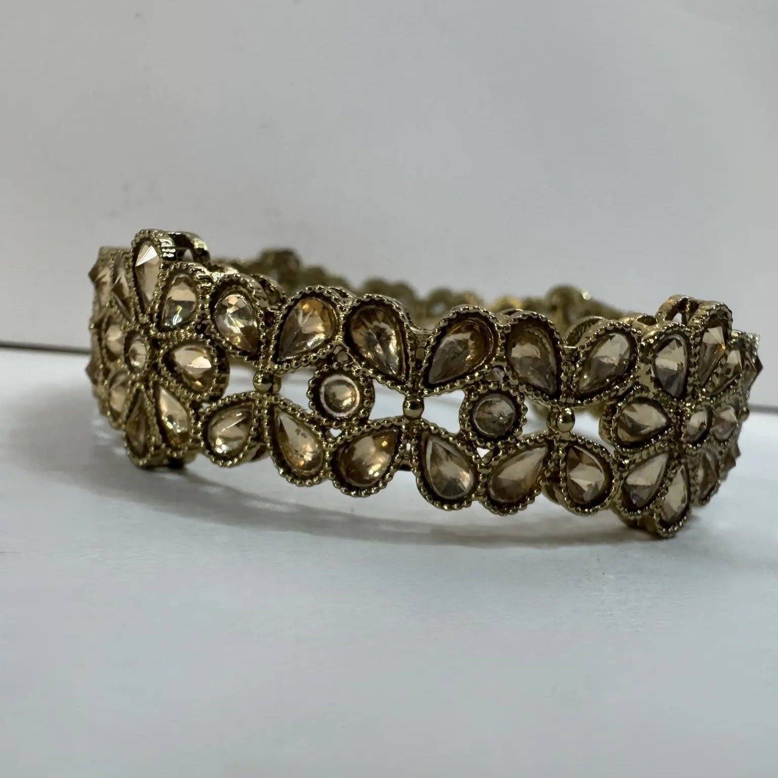 Gold plated bangle with clear gemstones and floral patterns on a light gray background