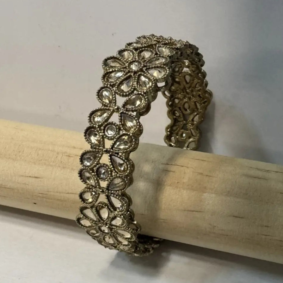 Gold plated bangle with clear gemstones on a wooden stick against a white background