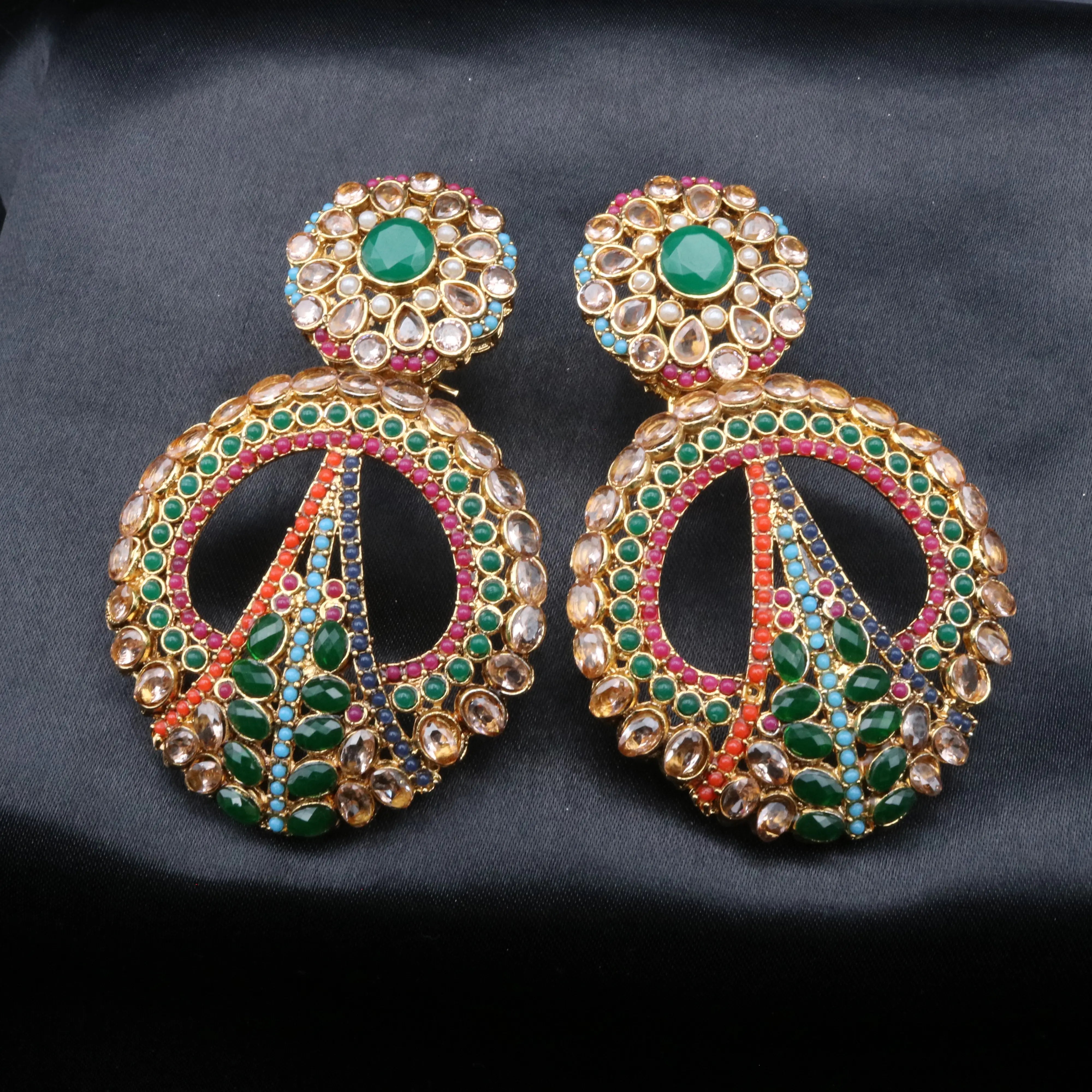 Ornate earrings with green and pink stones on a dark background