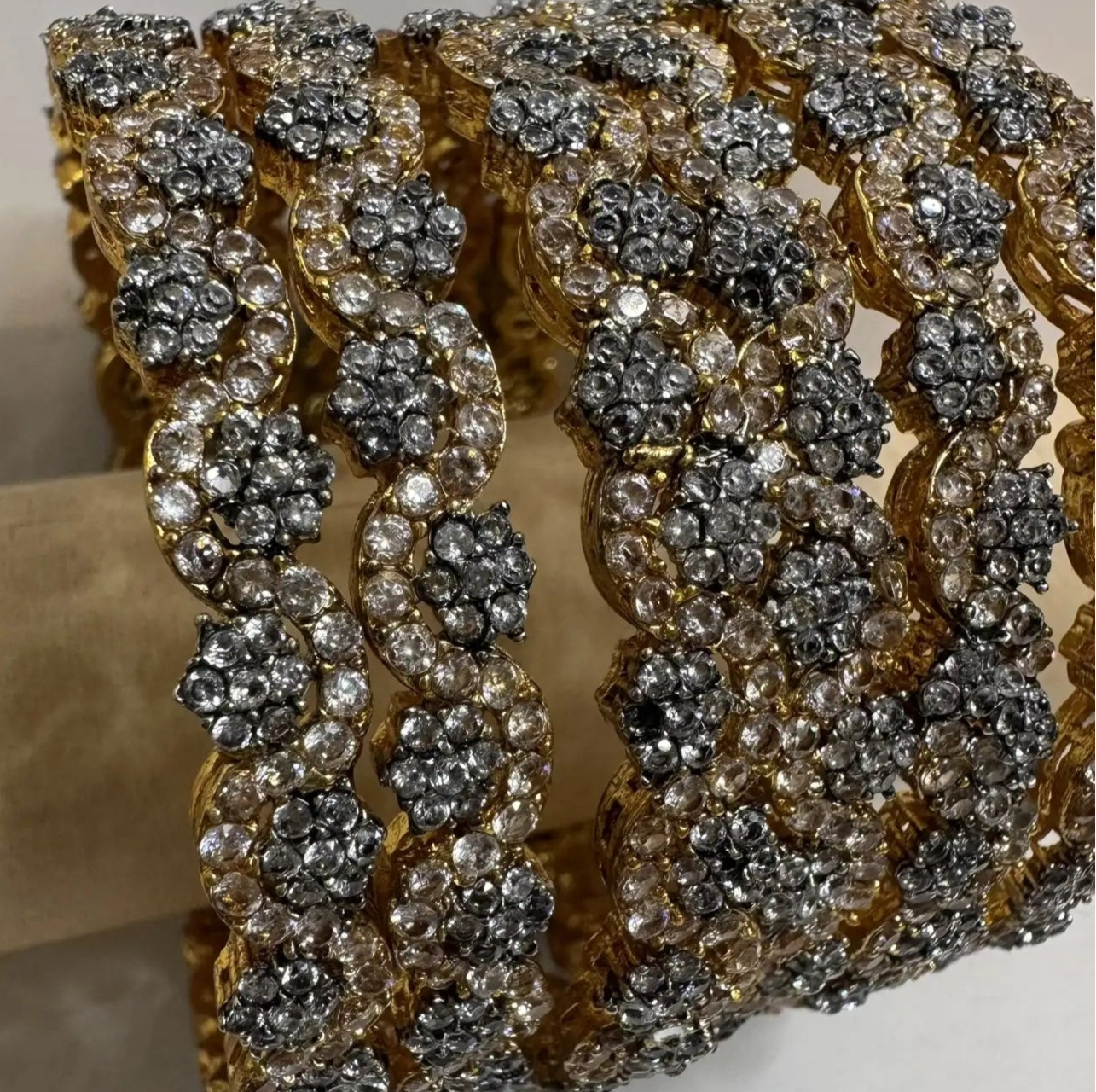 gold plated bangles with floral patterns with silver embellishments on a white surface and wood stick